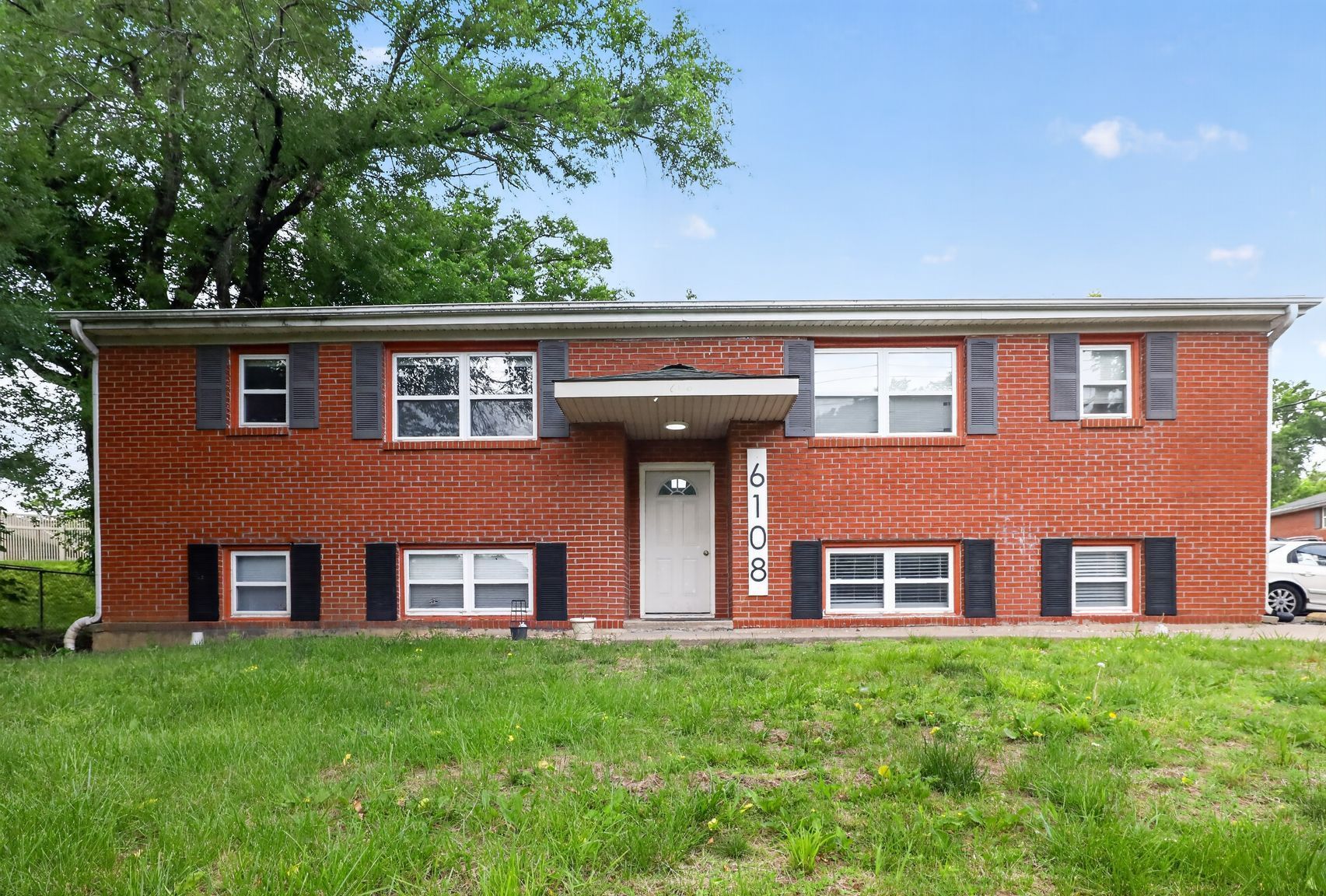 A two-story apartment building with beige siding and dark balconies, surrounded by dormant trees and landscaping.