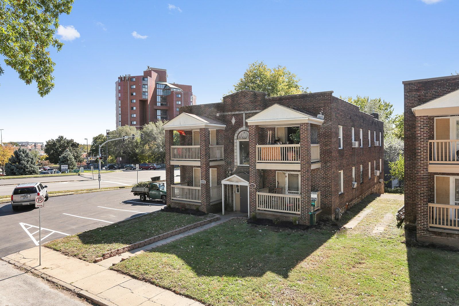 A two-story apartment building with beige siding and dark balconies, surrounded by dormant trees and landscaping.