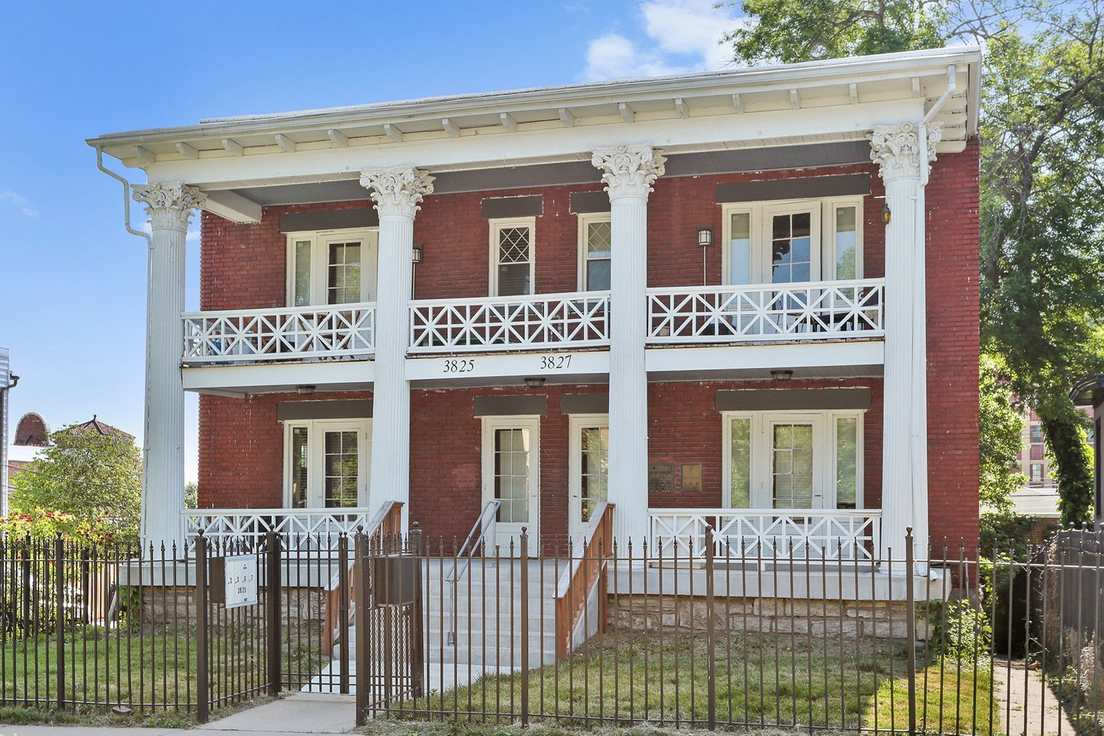 A two-story apartment building with beige siding and dark balconies, surrounded by dormant trees and landscaping.
