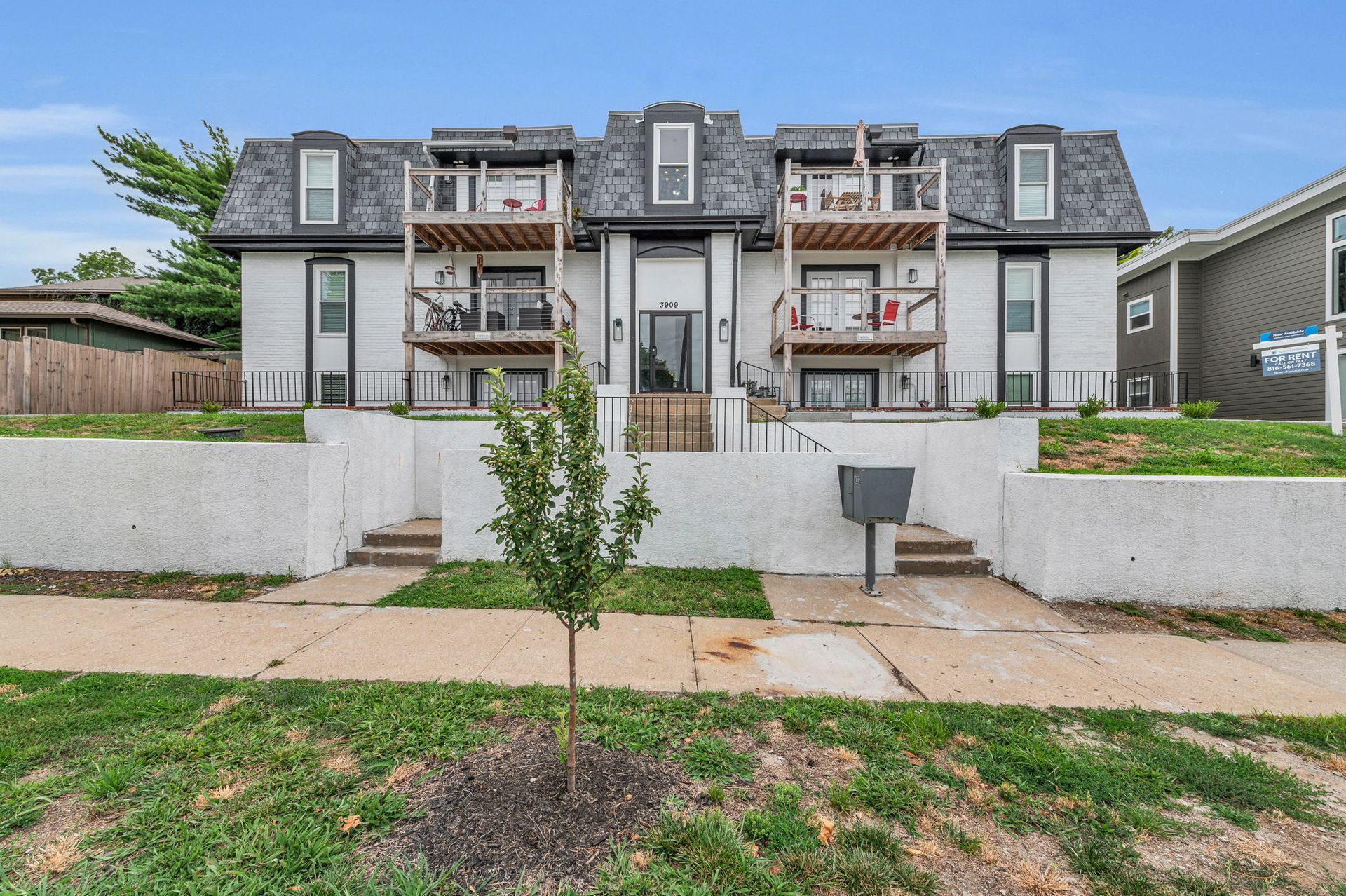 A two-story apartment building with beige siding and dark balconies, surrounded by dormant trees and landscaping.