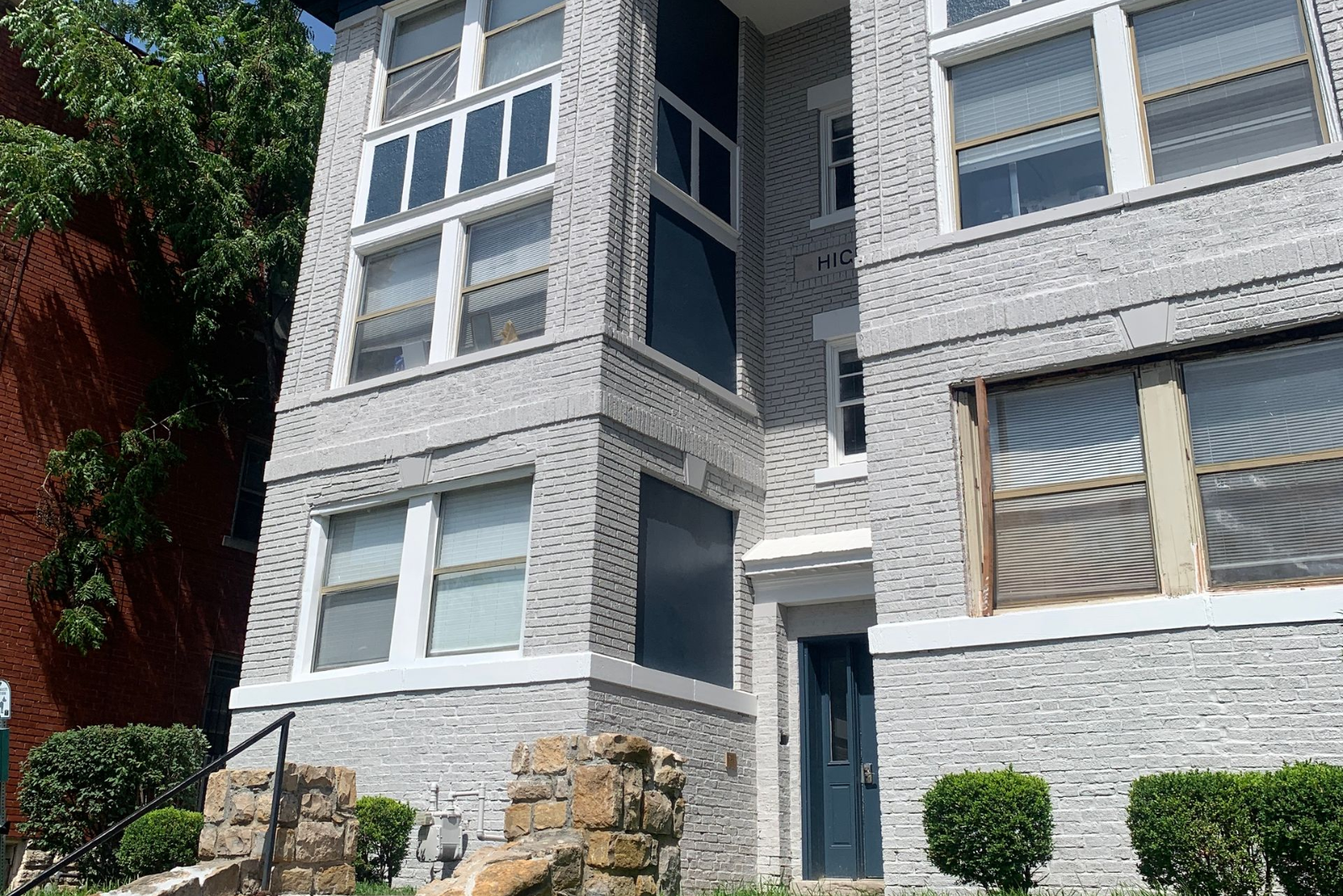 A two-story apartment building with beige siding and dark balconies, surrounded by dormant trees and landscaping.