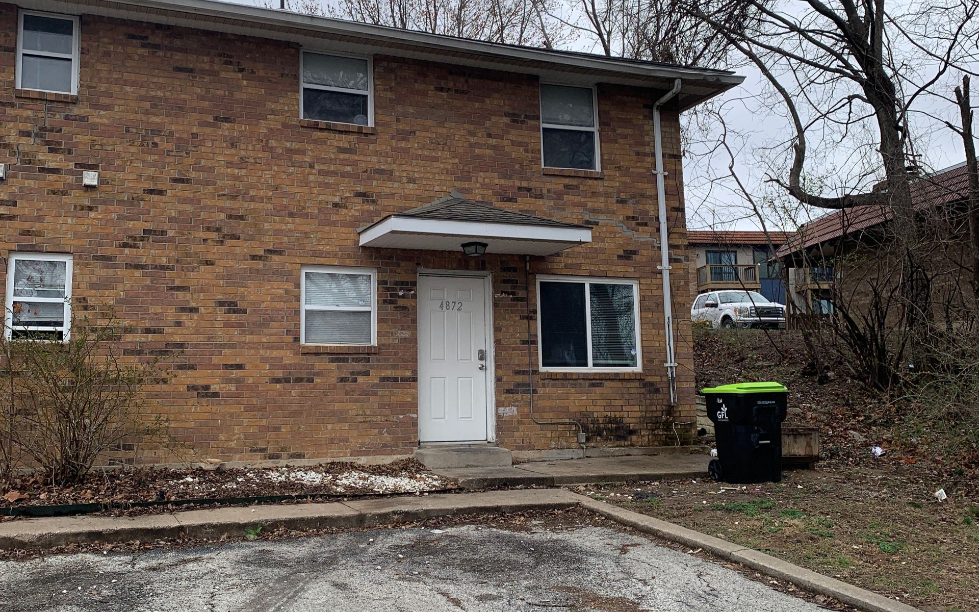 Two-story brick apartment building with four units, brown doors, green lawn, and clear sky.