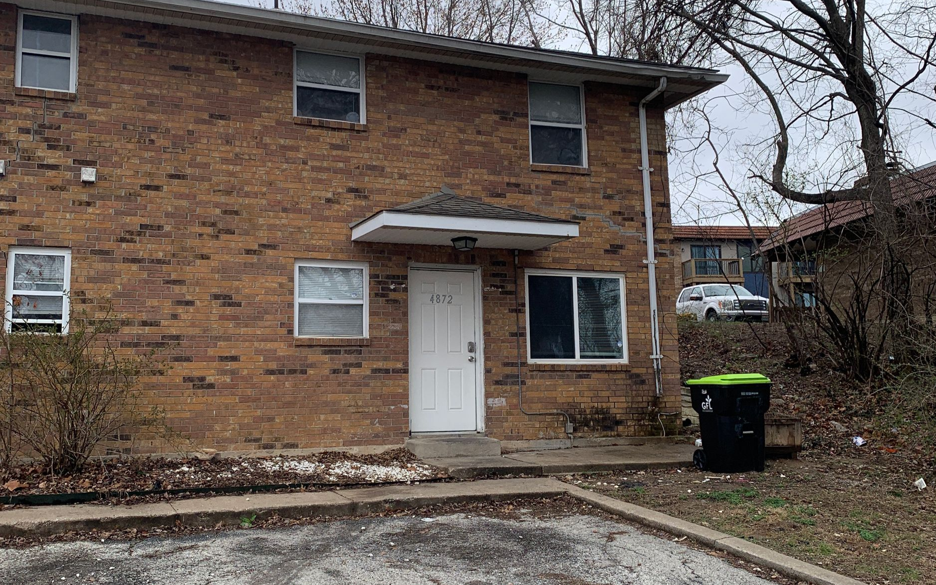 Two-story brick apartment building with four units, brown doors, green lawn, and clear sky.