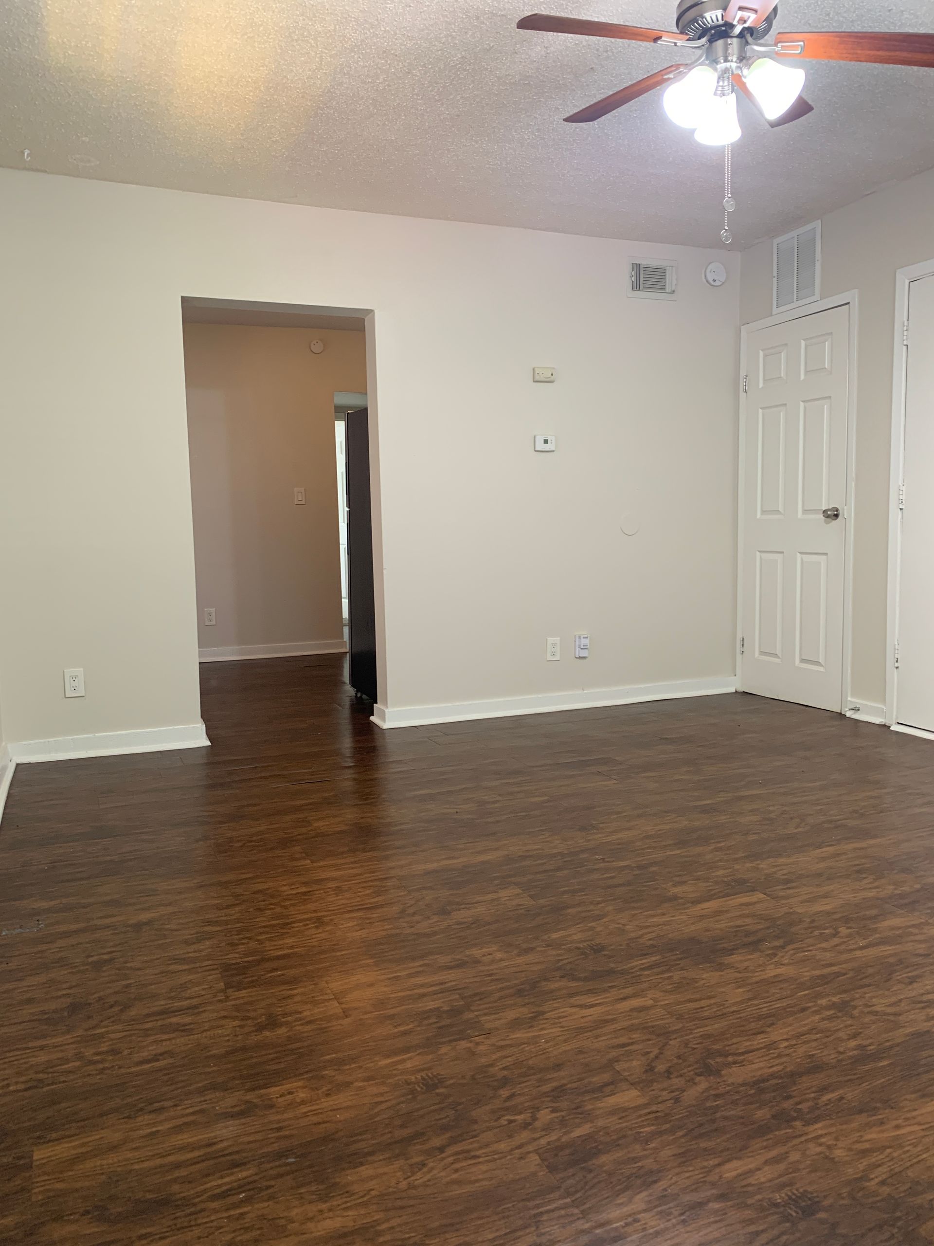 Empty room with dark wood-look flooring, white walls, and a ceiling fan.