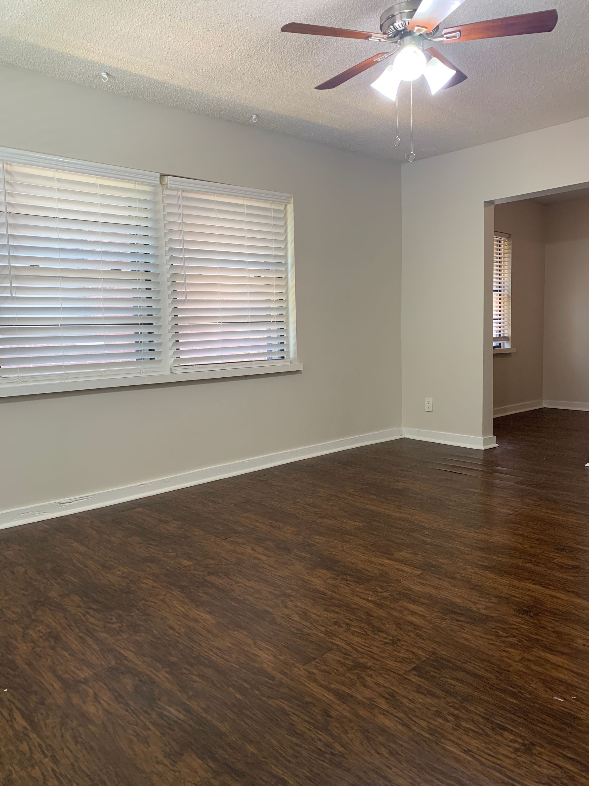 Empty room with wood-look flooring, light gray walls, window with blinds, and ceiling fan.