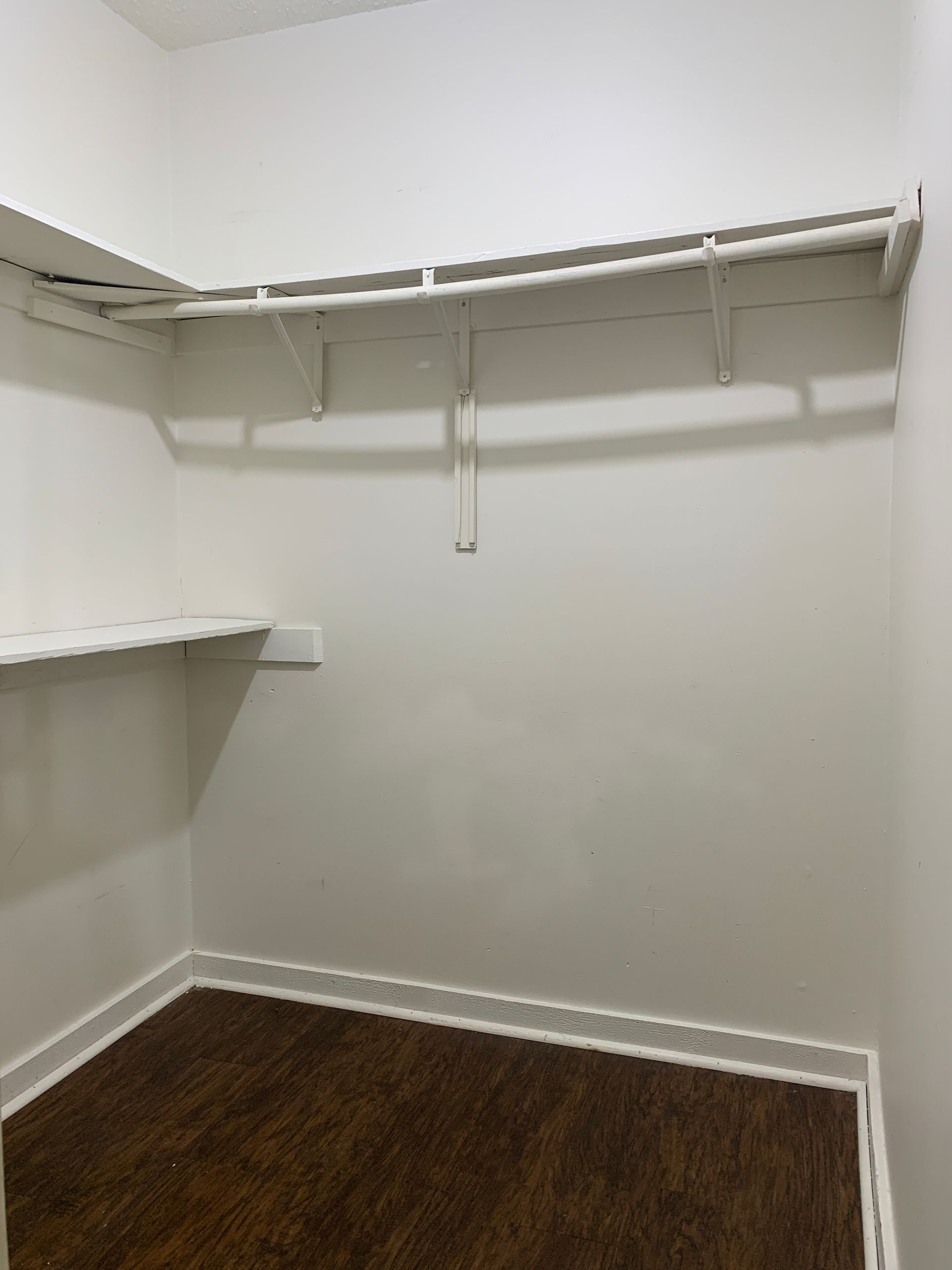 Empty white closet with shelves and a rod, brown floor.