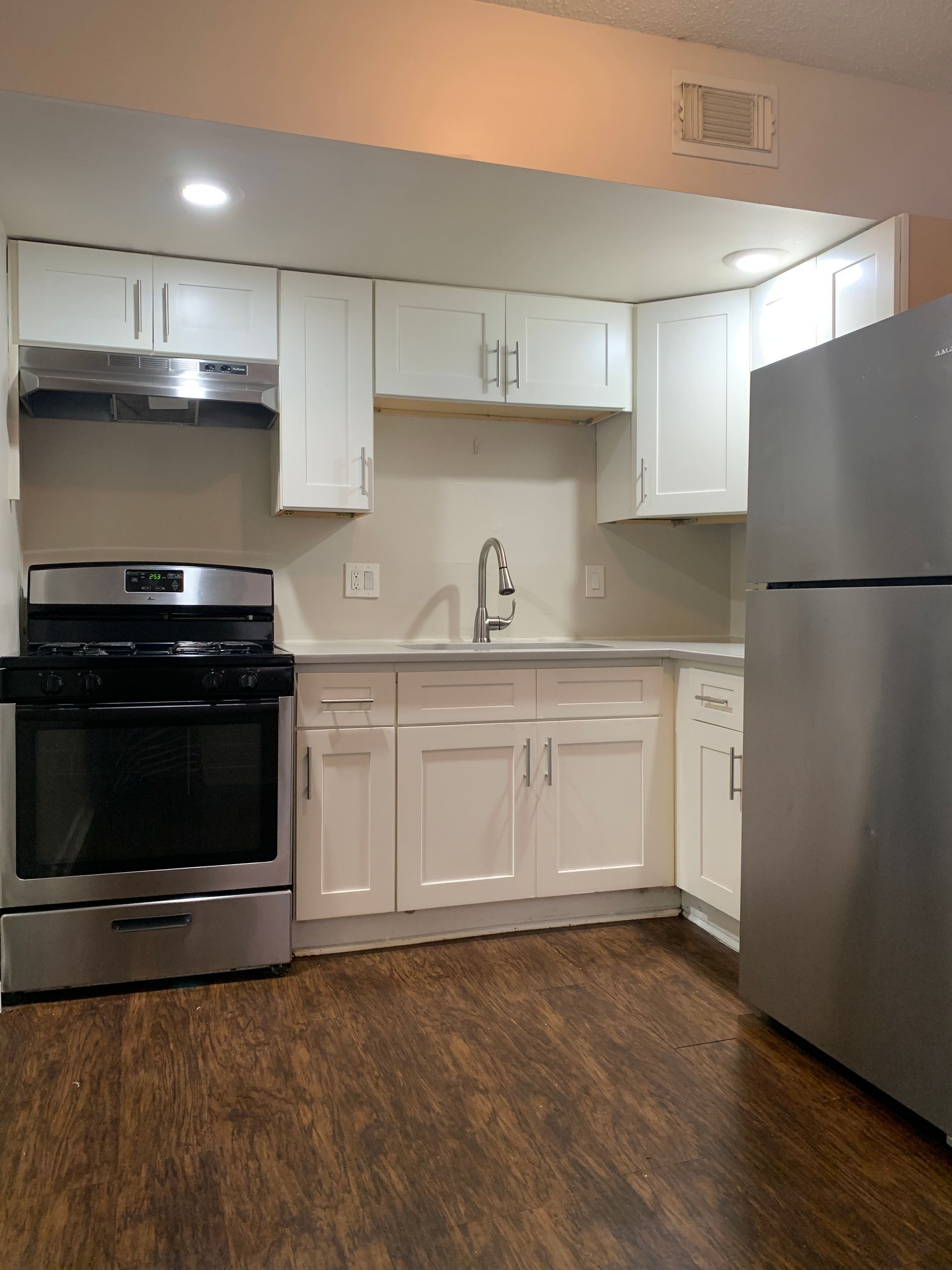 White kitchen cabinets, stainless steel appliances, dark wood-look floor, and light-colored walls.