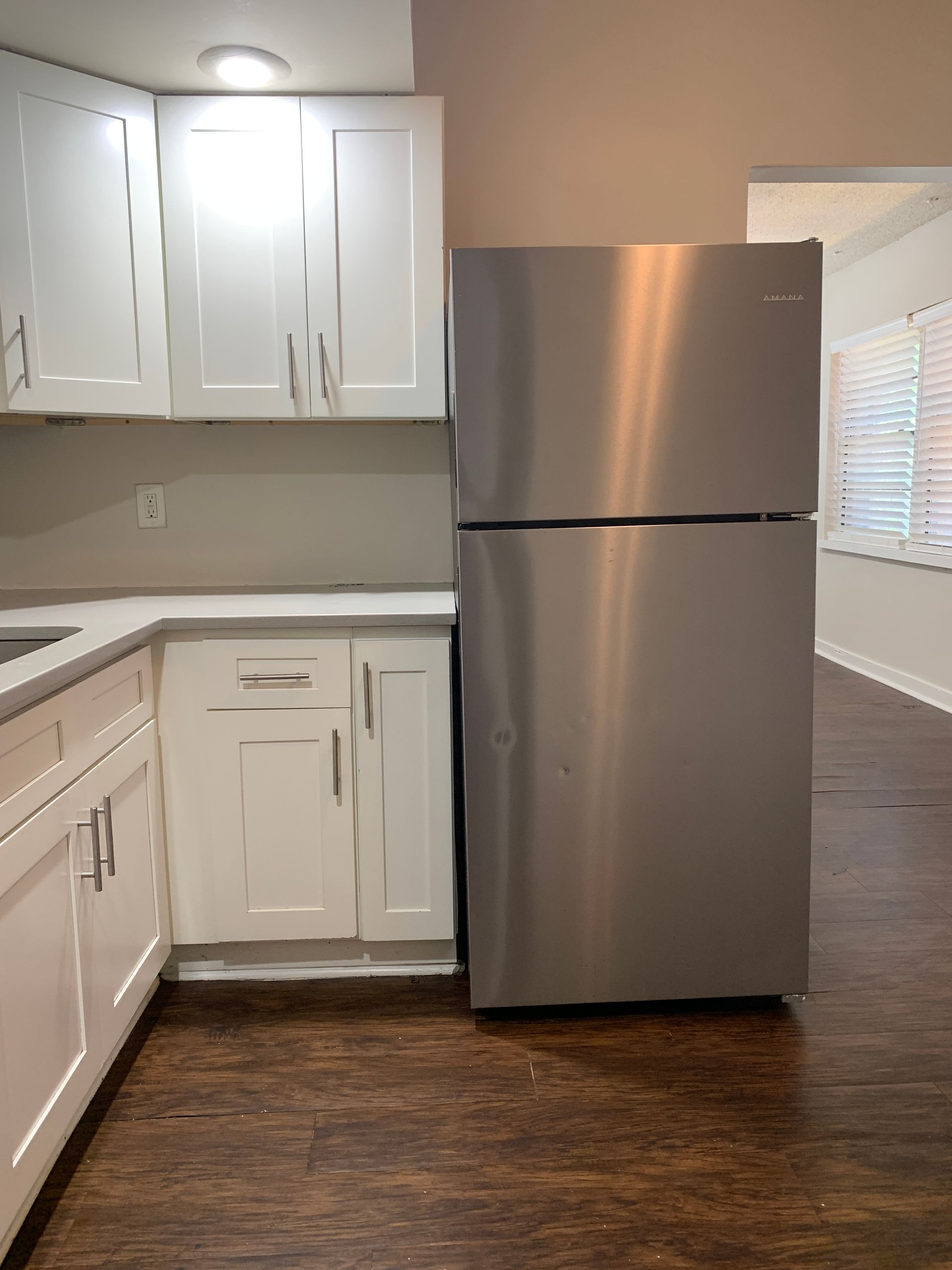 Stainless steel refrigerator next to white kitchen cabinets and countertop in a room with hardwood floors.