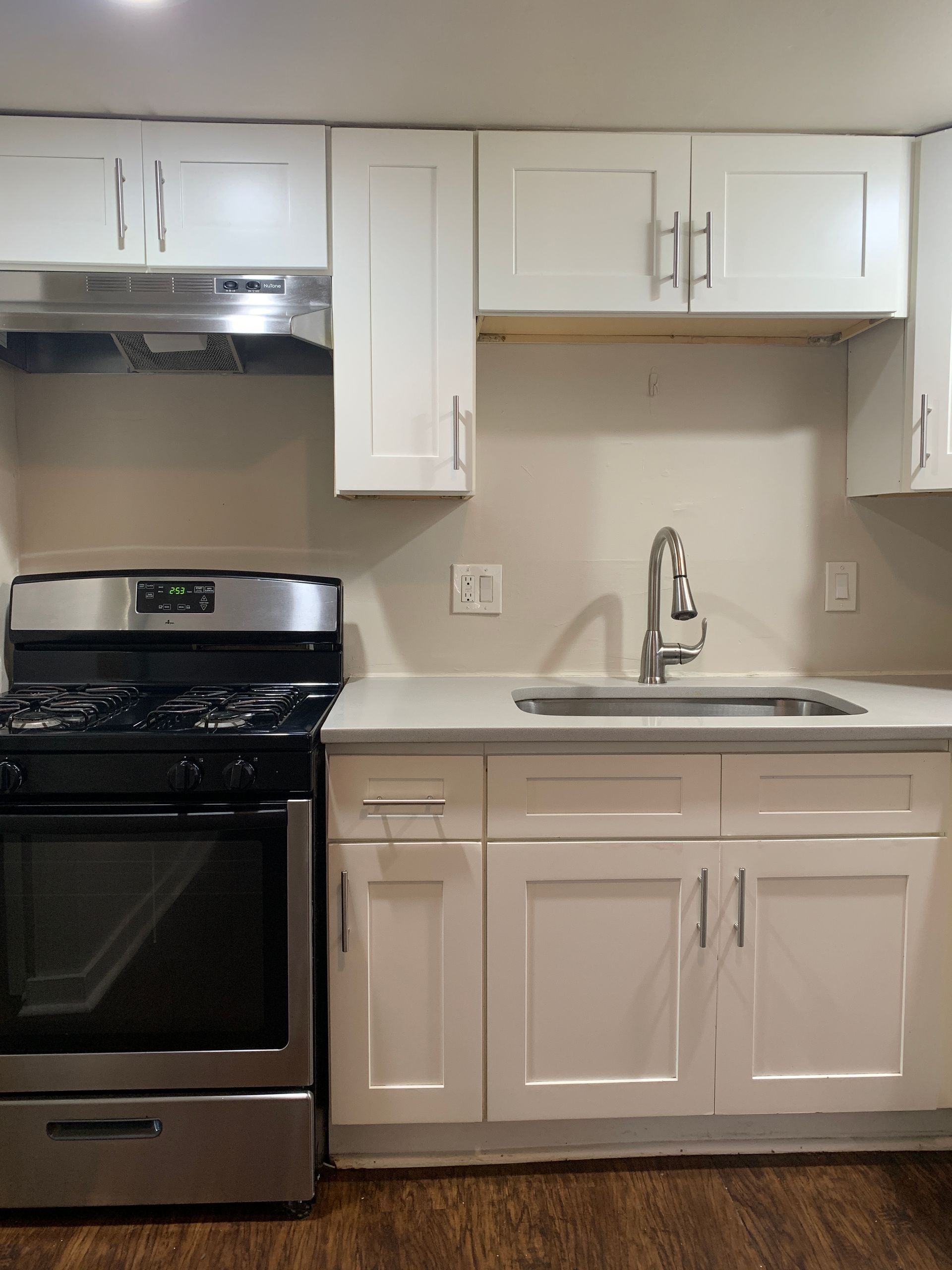 White kitchen cabinets, stainless steel oven, sink with faucet, and range hood.