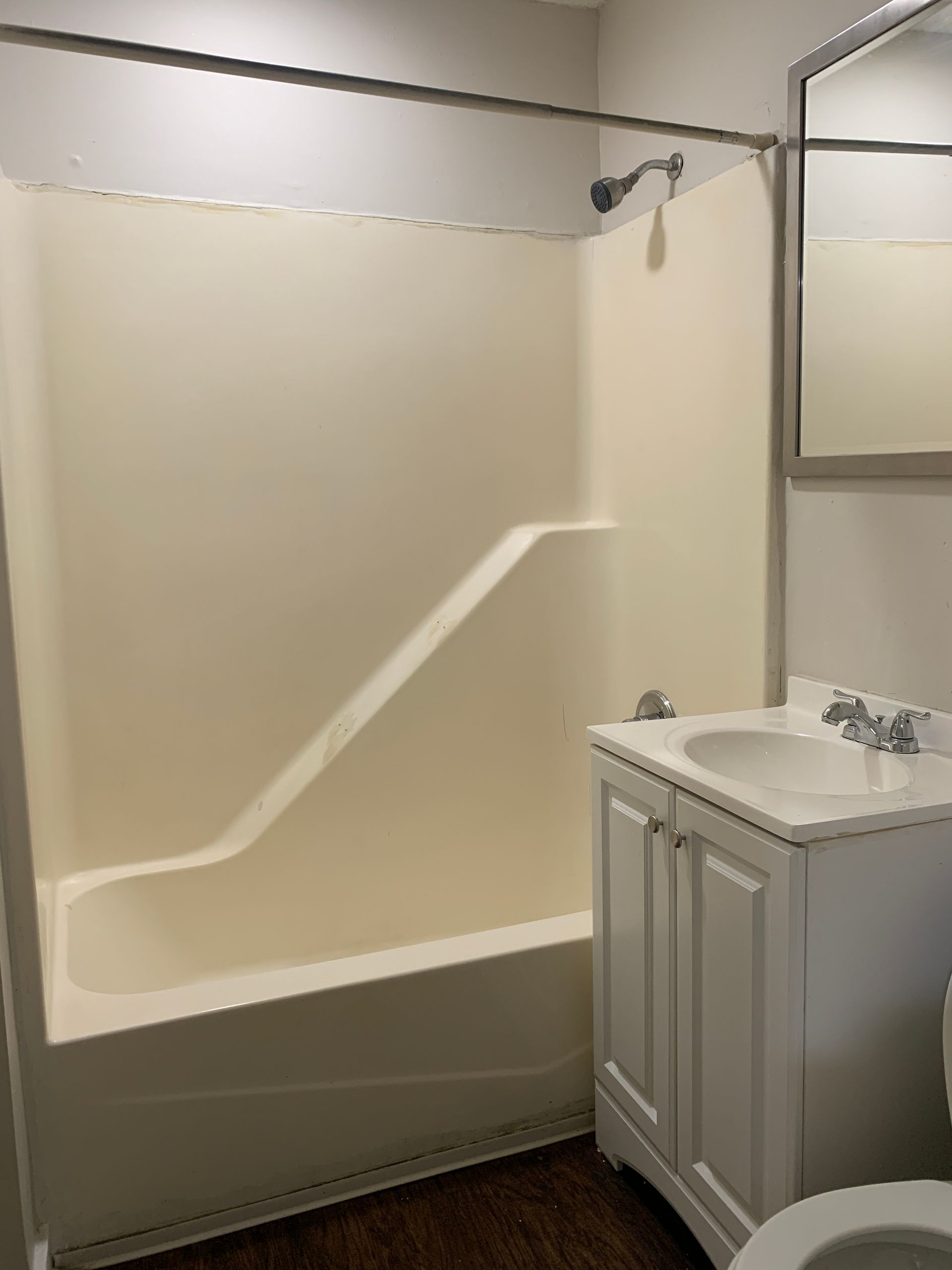 Bathroom with a white tub, sink, and cabinet; a silver shower head, and a dark floor.