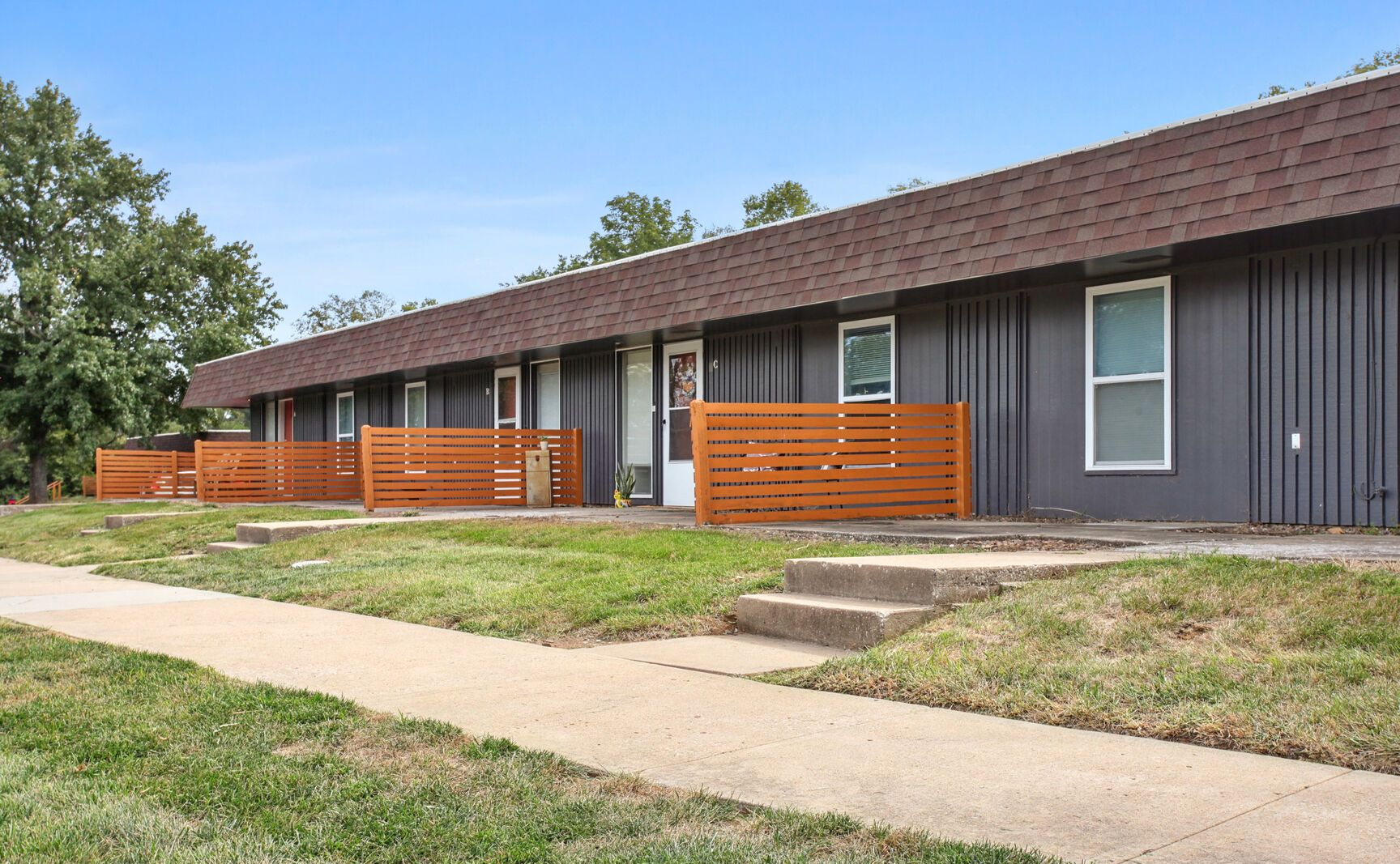 Row of gray townhouses with brown roofs and wooden fences.