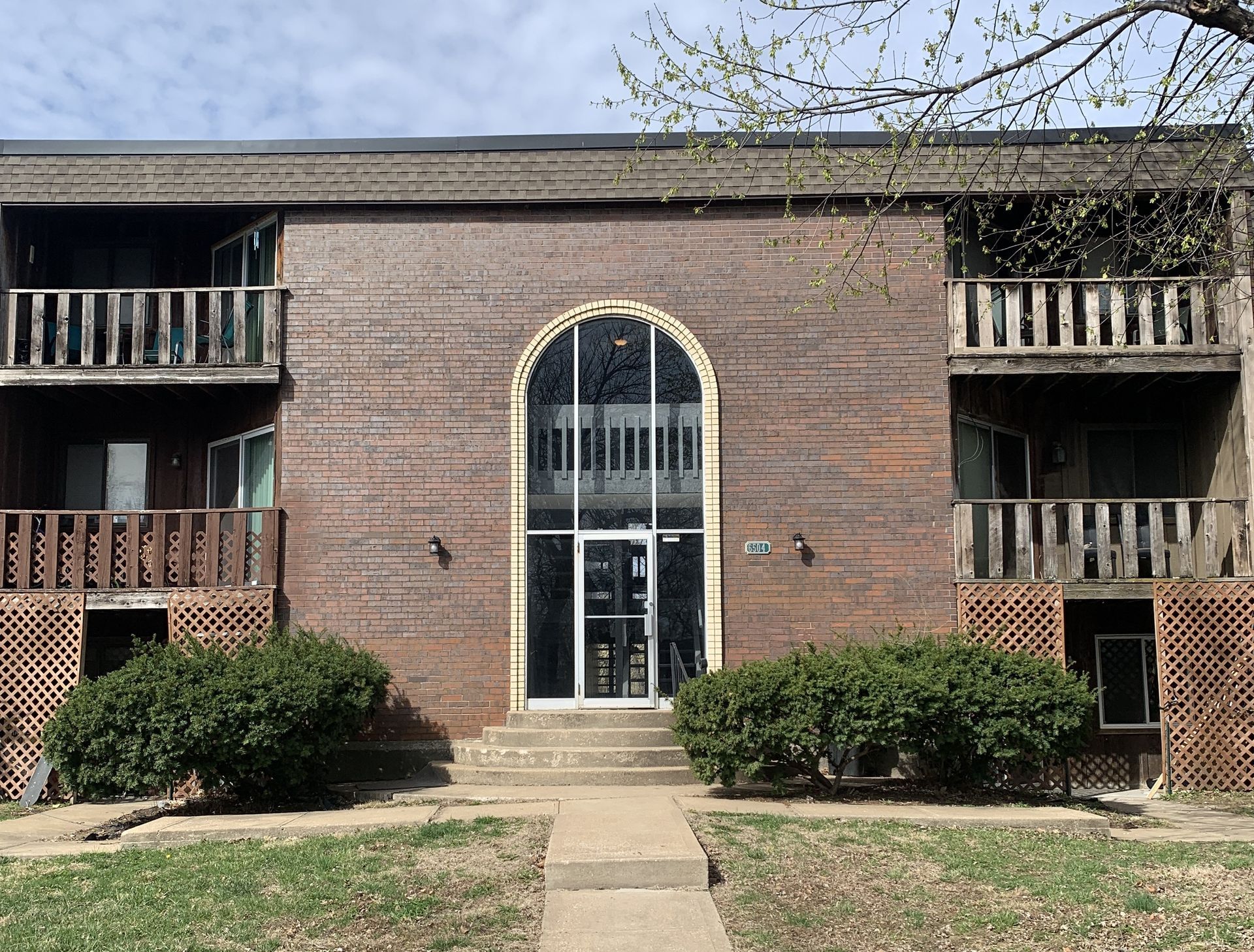 Brick apartment building with arched entrance, balconies, and bushes.