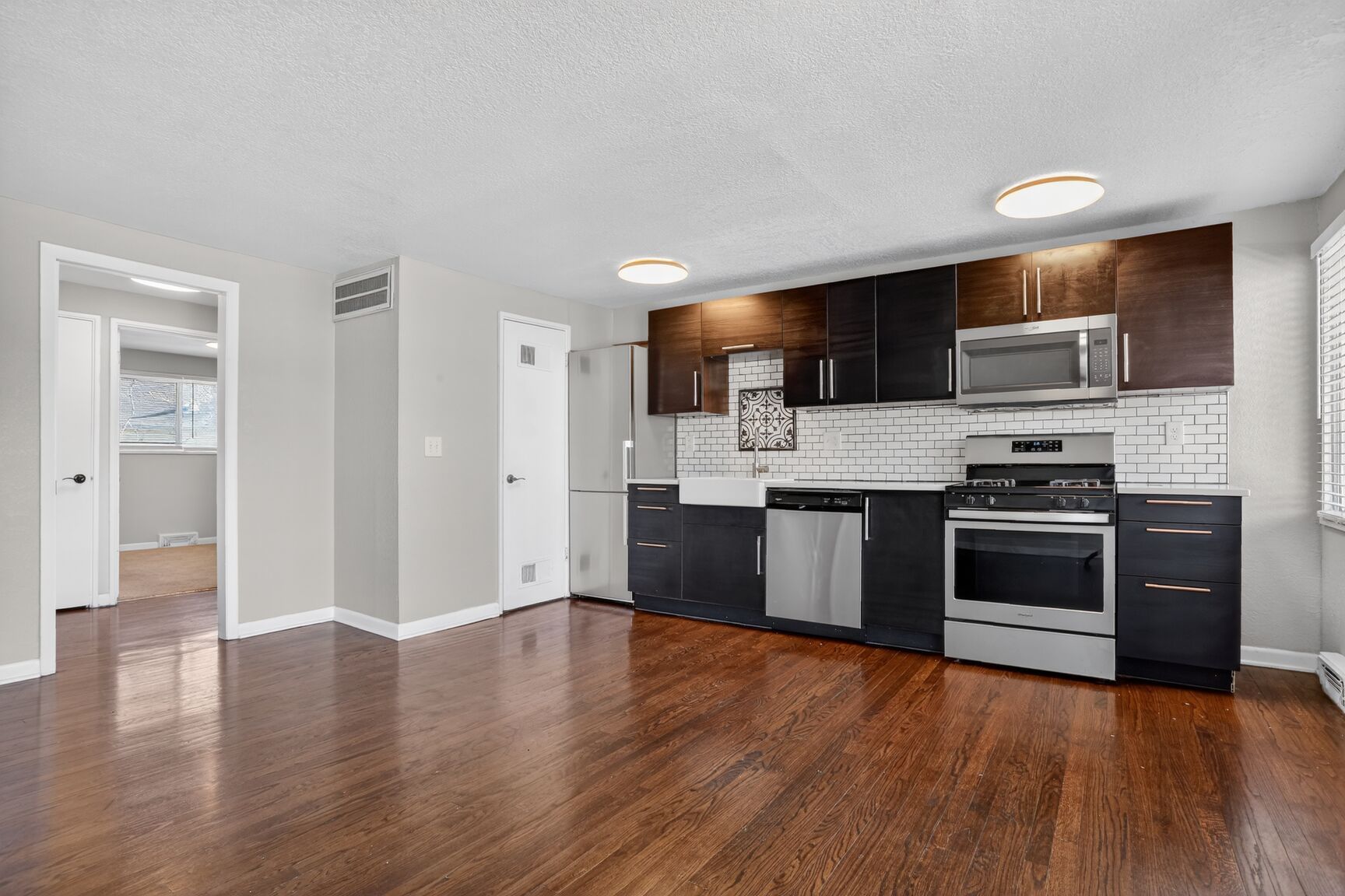 Modern kitchen with dark wood cabinets, stainless steel appliances, and wood floors in an open-concept living area.