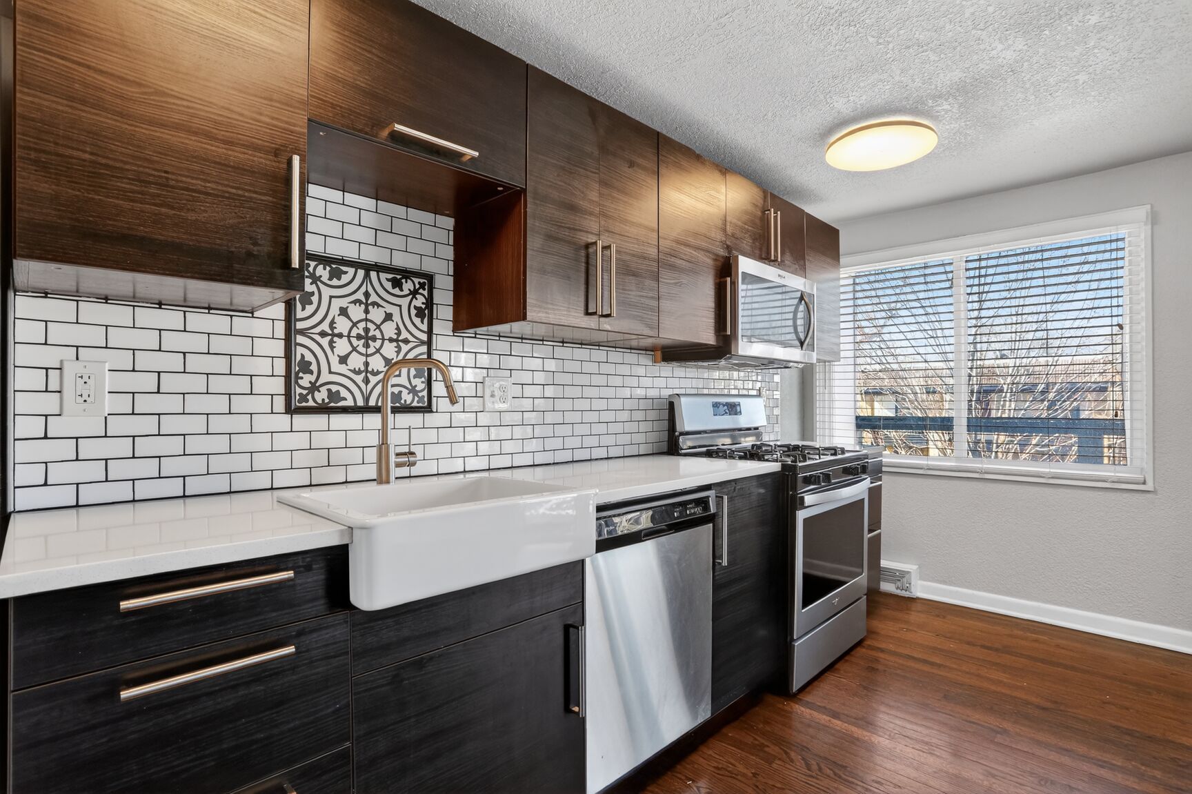 A modern kitchen with dark wood cabinets, a white farmhouse sink, white subway tile backsplash, and stainless appliances.