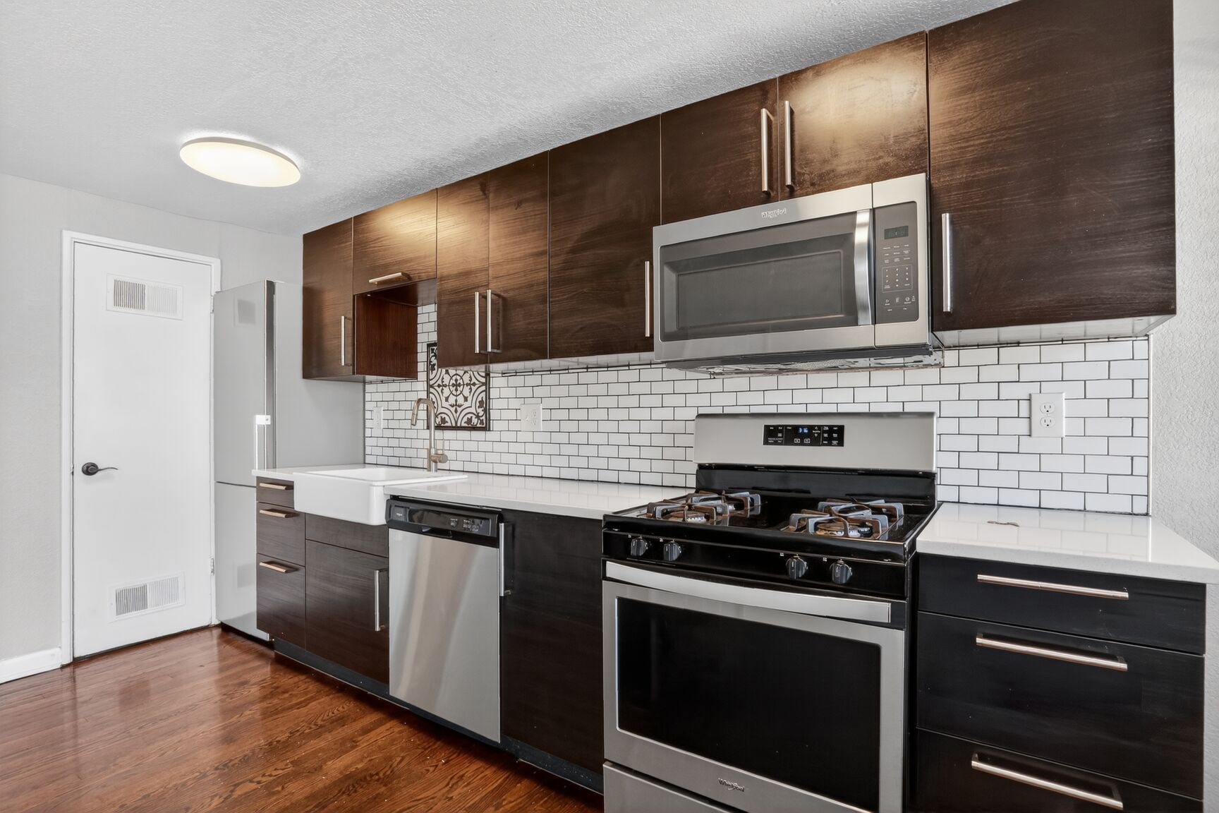 A modern kitchen featuring dark wood cabinets, stainless steel appliances, white subway tile backsplash, and wood floors.