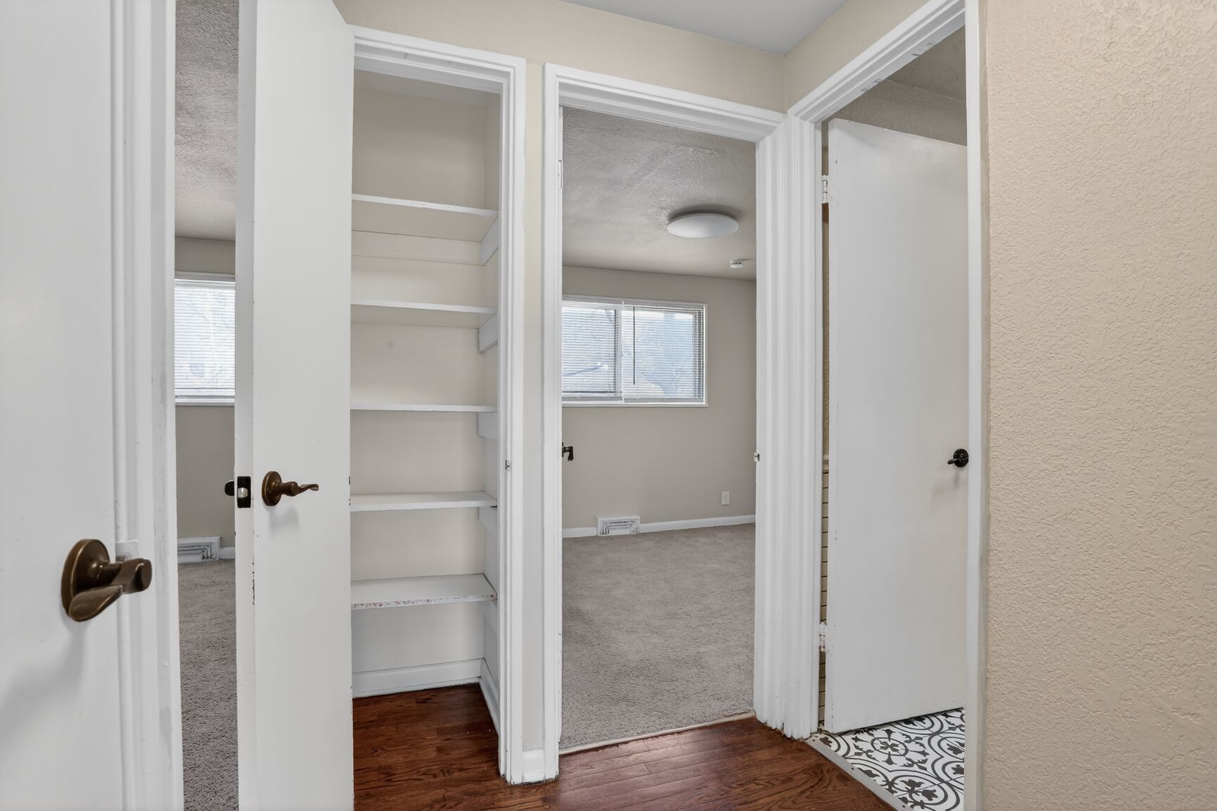 Hallway with wooden floors, white doors, a built-in shelving unit, and views into carpeted rooms with windows.
