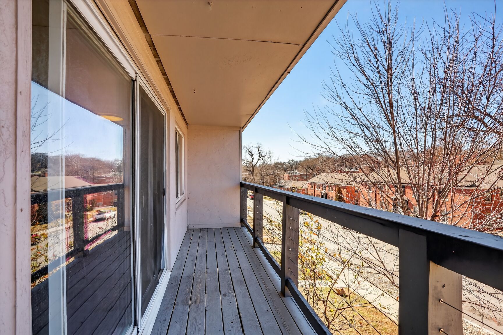 A view from a second-story apartment balcony overlooking a street, trees, and neighboring houses on a sunny day.