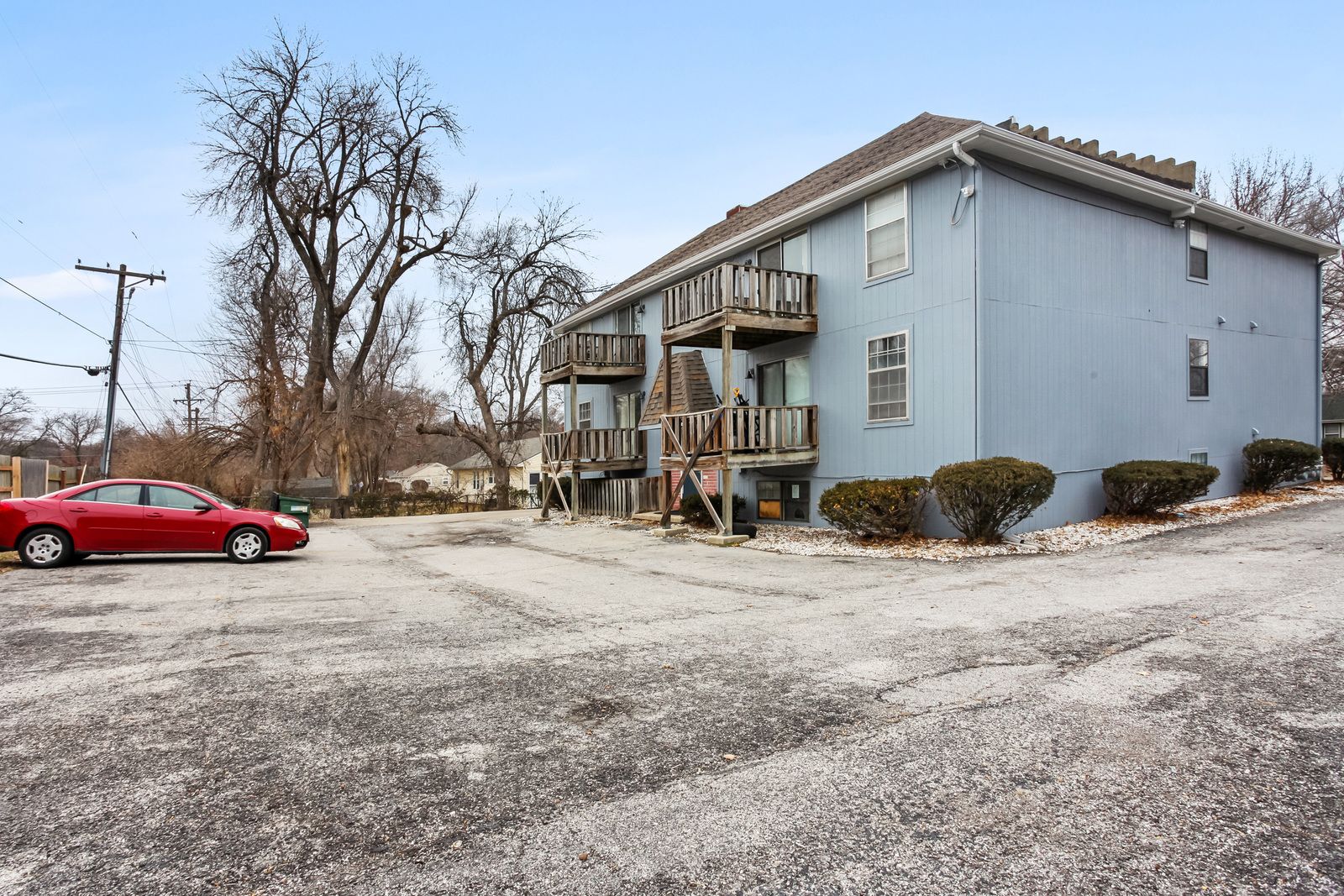 Blue two-story apartment building with balconies, gray gravel parking lot, and a red car.
