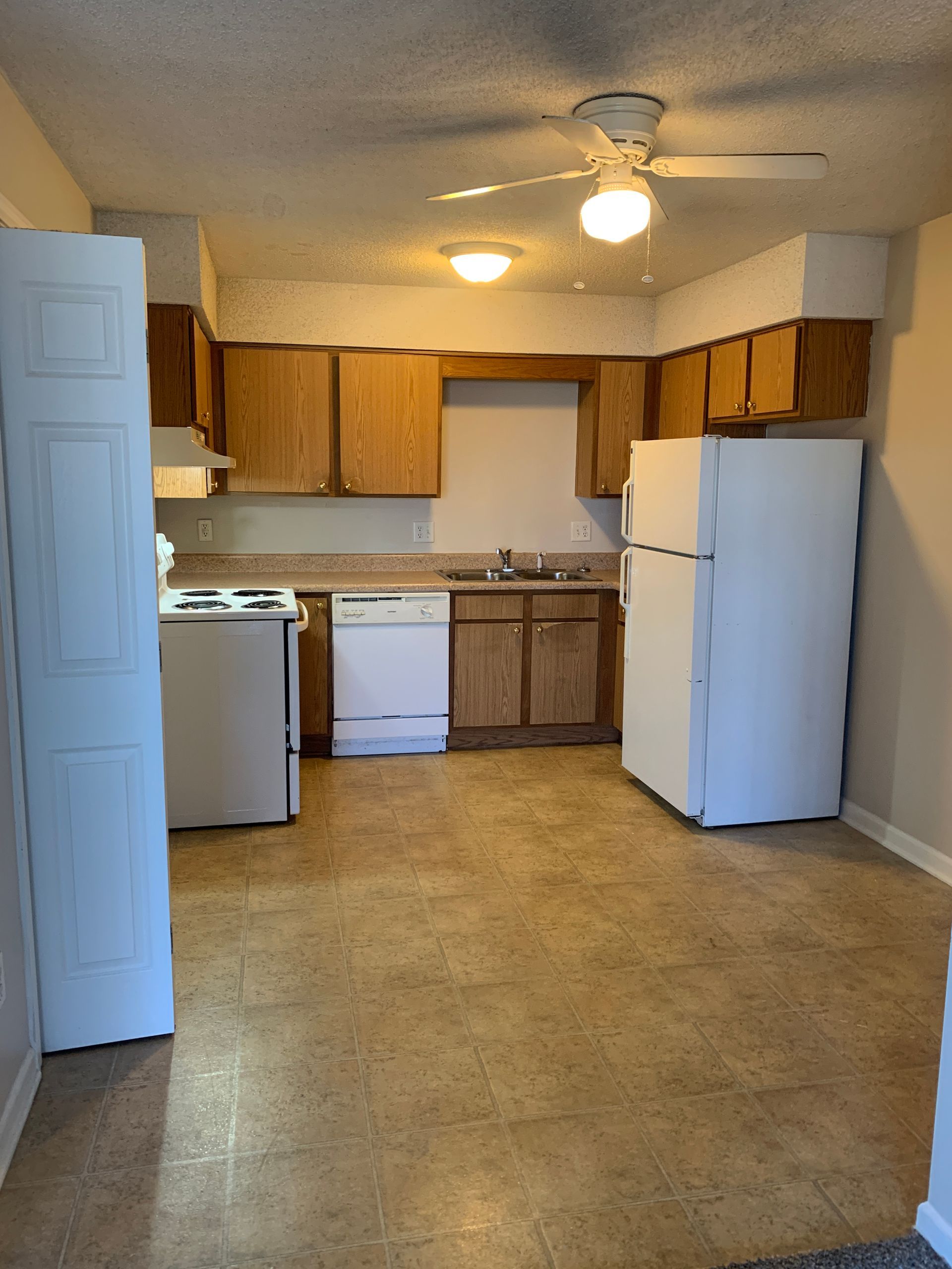Kitchen with wooden cabinets, white appliances, and tan flooring.