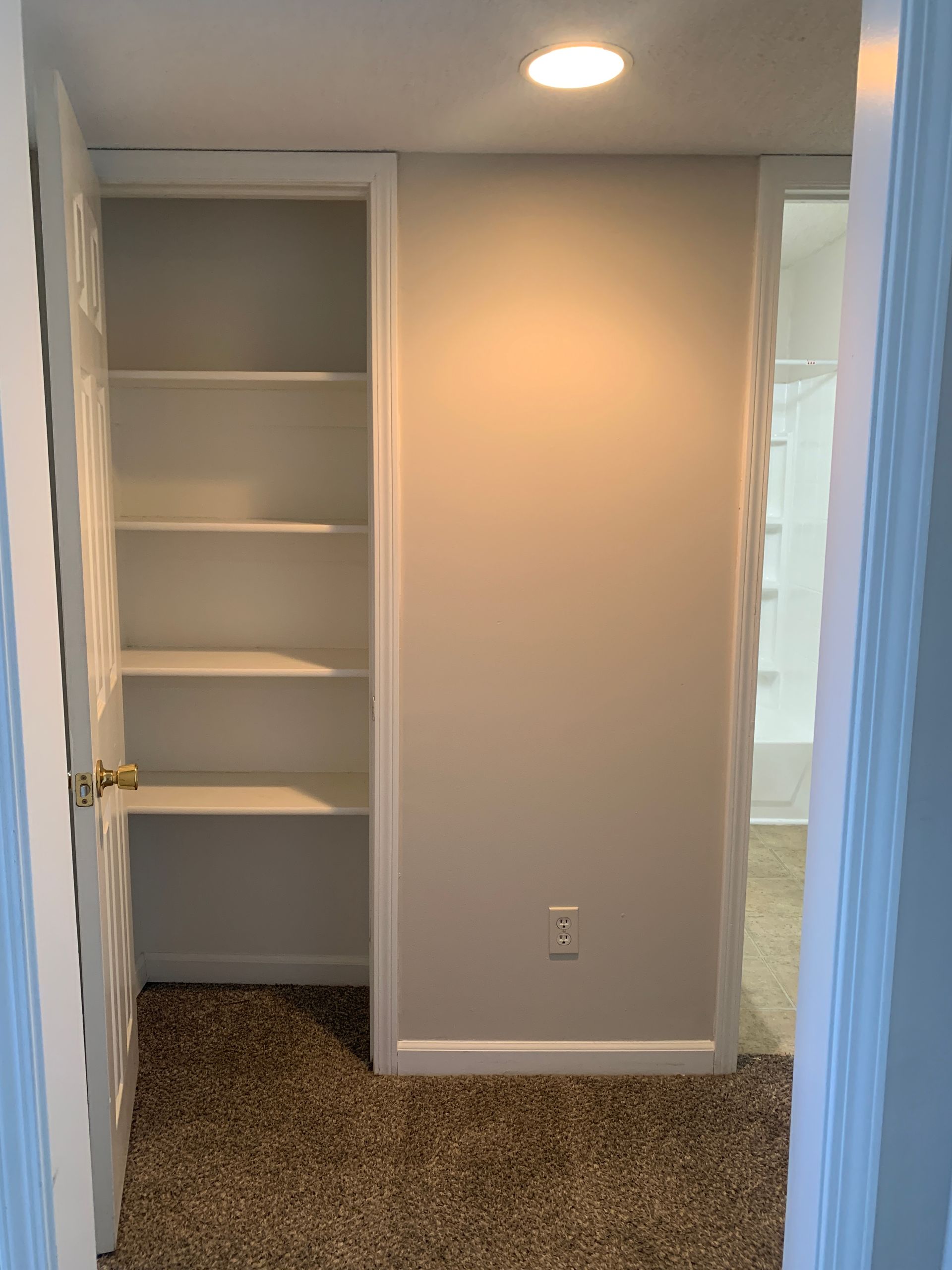 A small room with a closet on the left, an open doorway on the right. Tan carpet and walls, white trim.