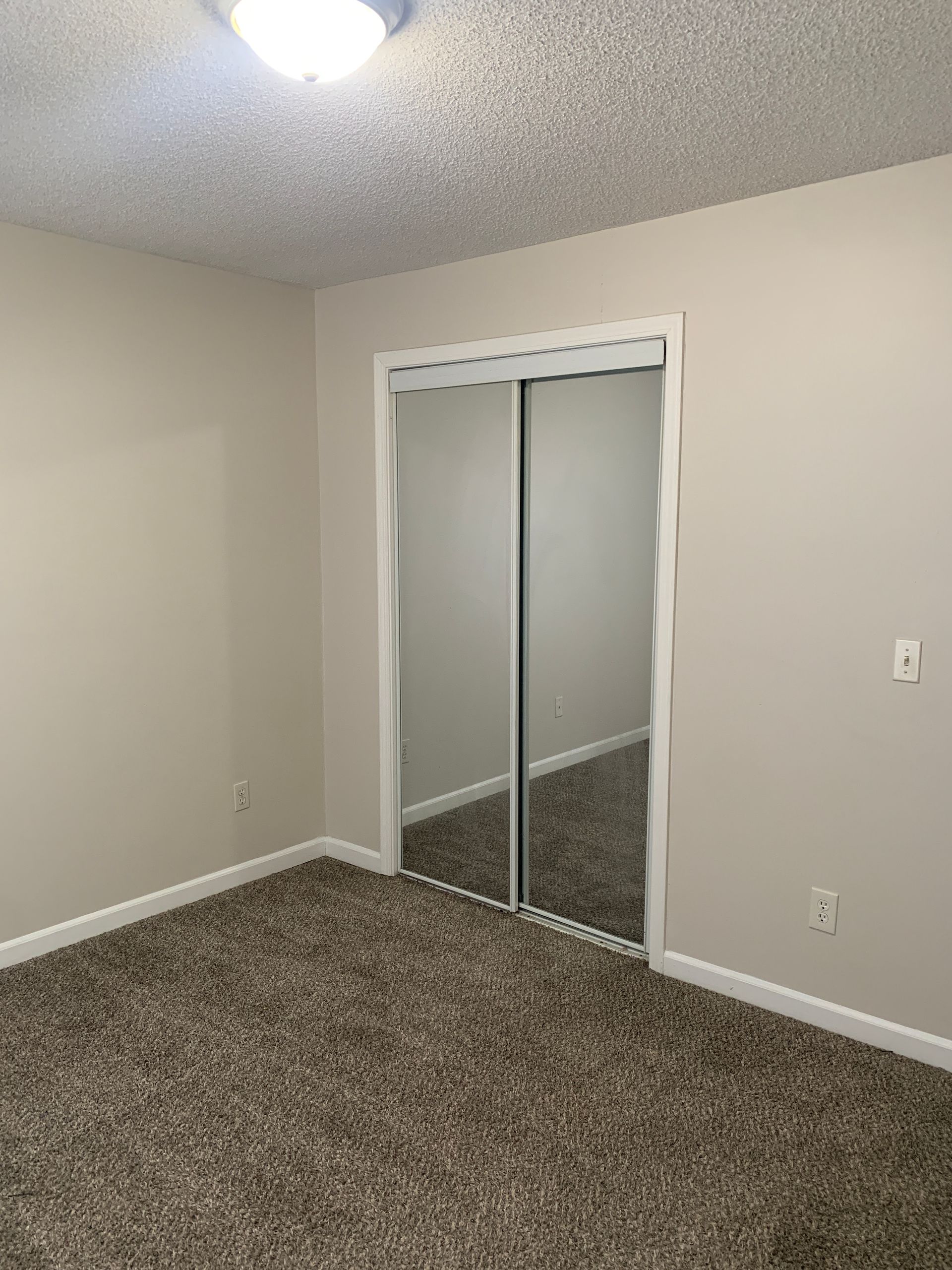 Empty bedroom with beige walls, brown carpet, and mirrored closet doors.