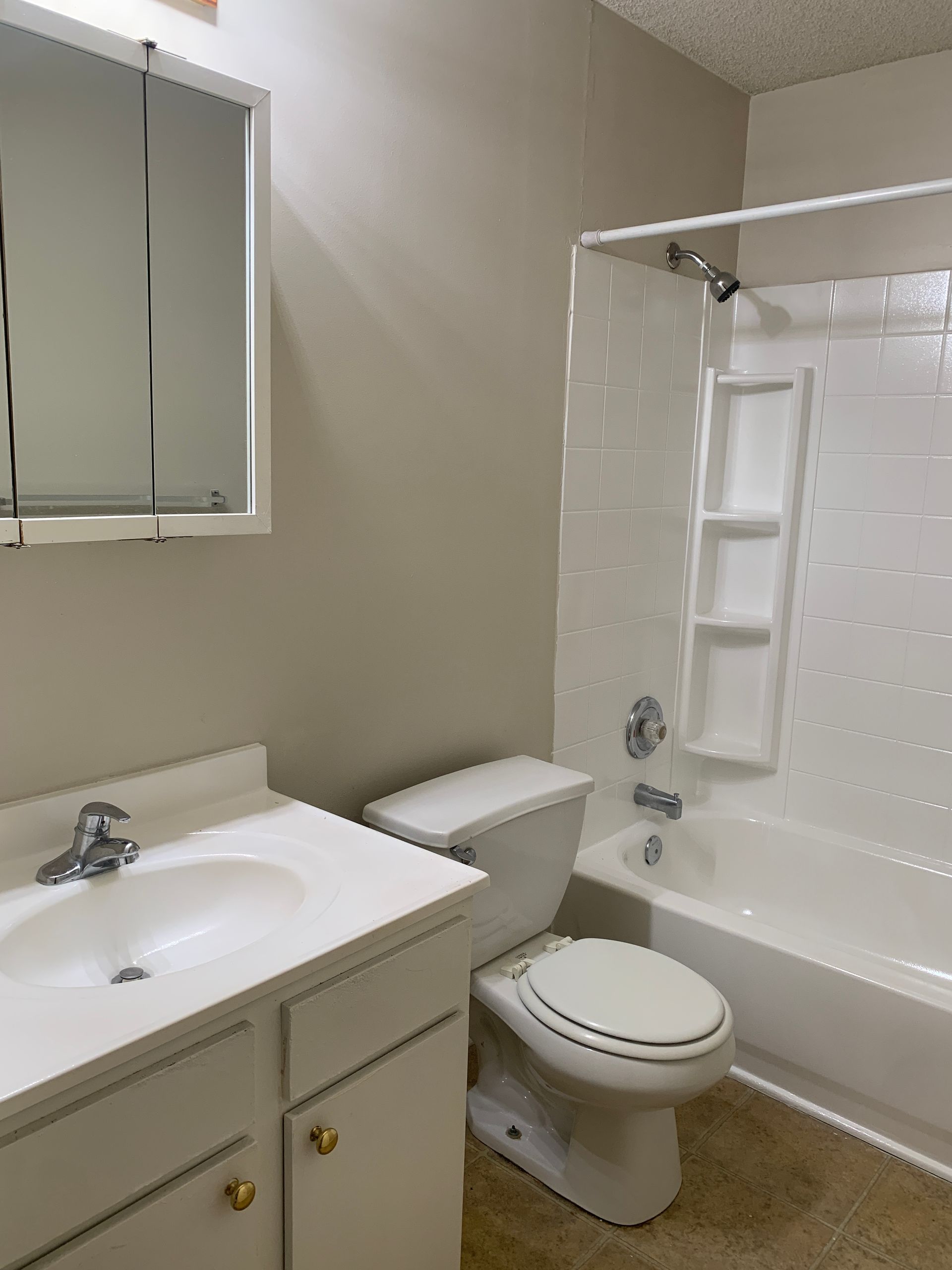 Bathroom with white sink, toilet, and bathtub. Beige walls, medicine cabinet above sink.