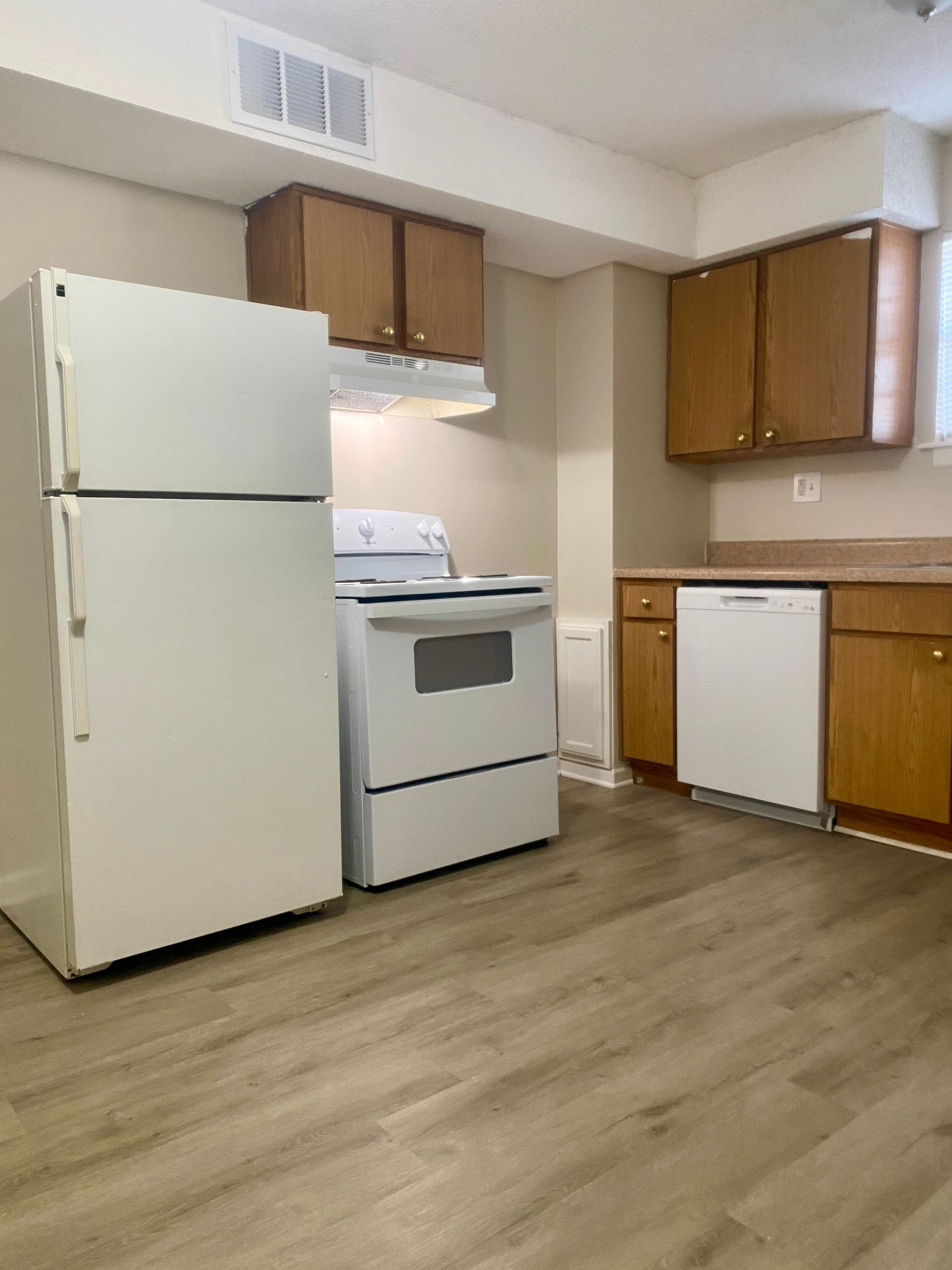 Kitchen with white appliances, brown cabinets, and light wood-look flooring.