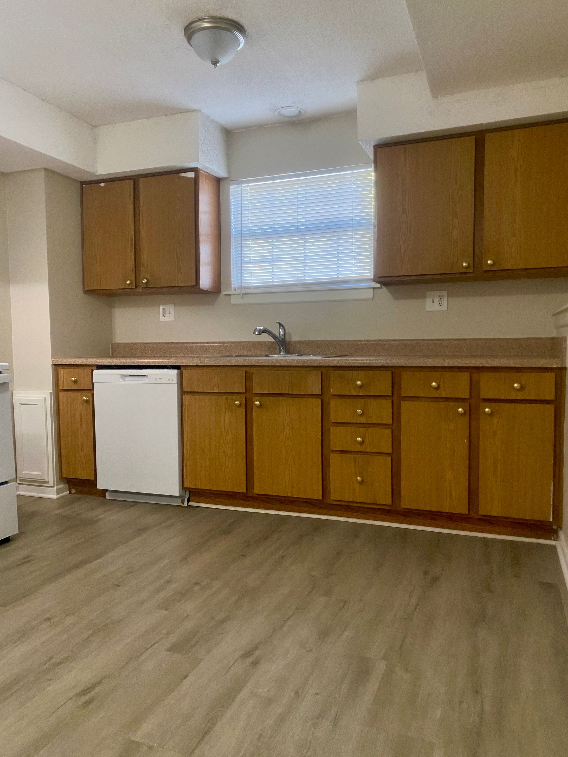 Kitchen with wooden cabinets, white appliances, and a window with blinds.