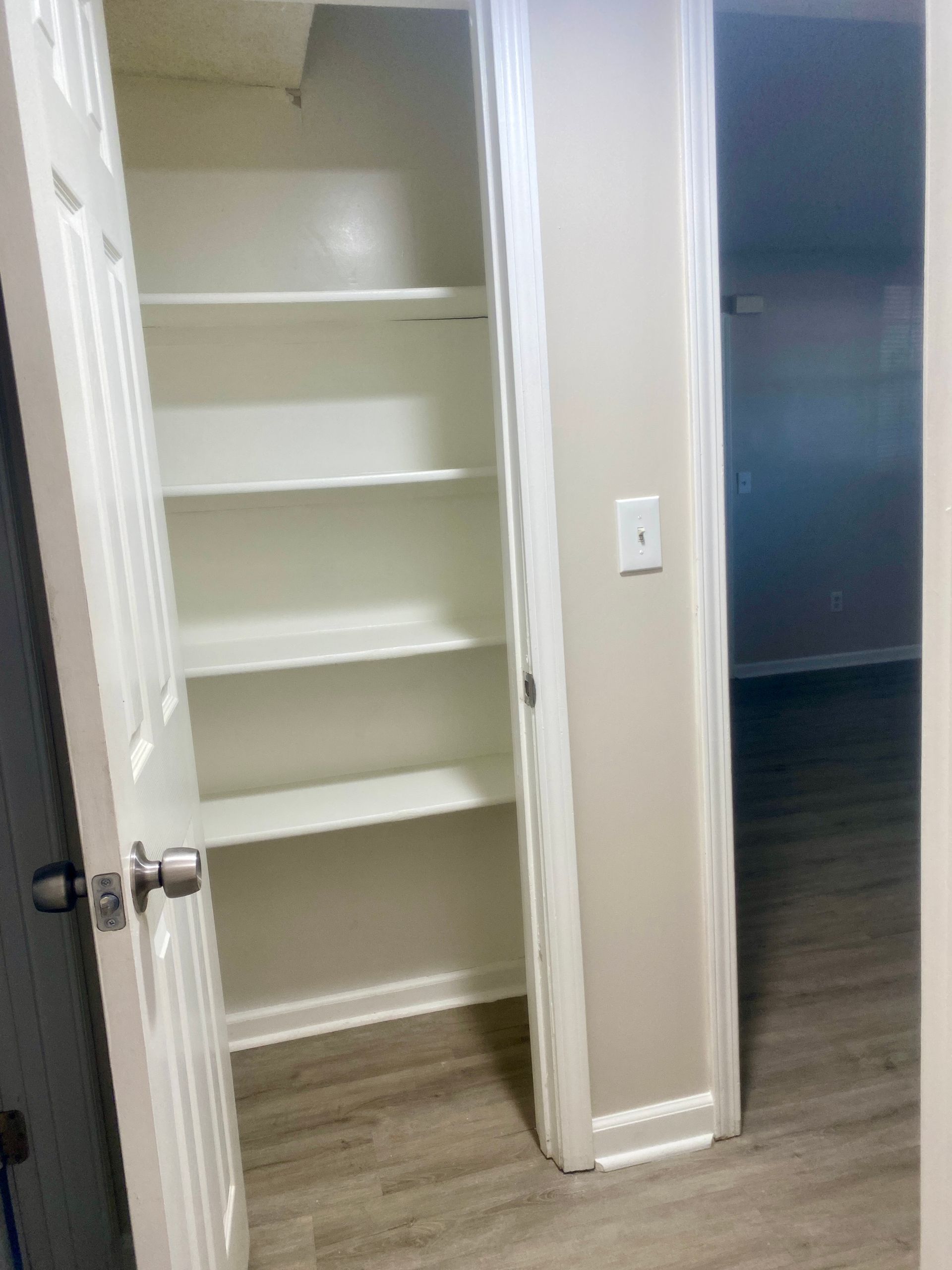 White closet with several shelves. The door is open, revealing wooden floors.