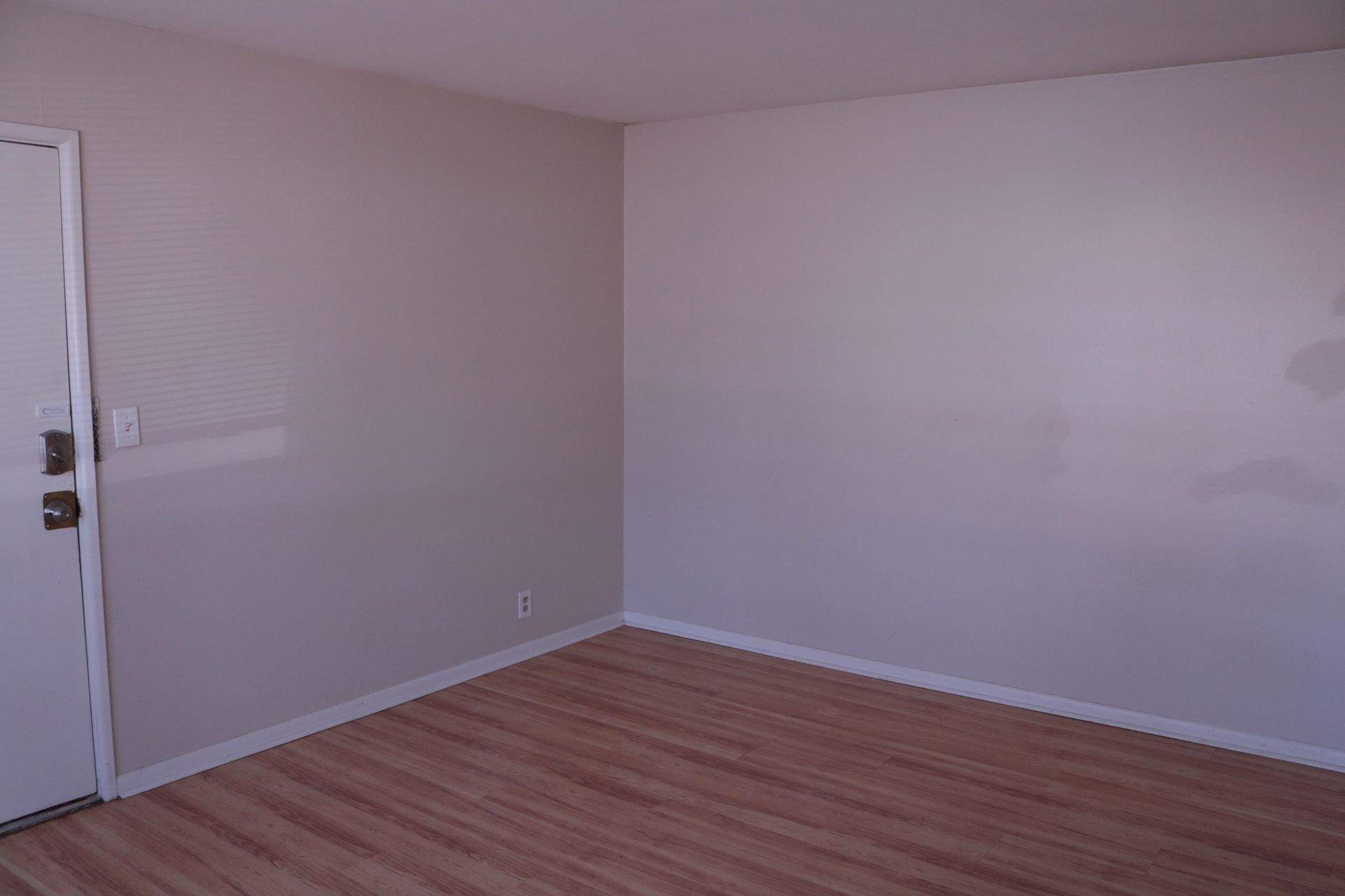 Empty room with light wood floor, painted walls, and a door on the left.