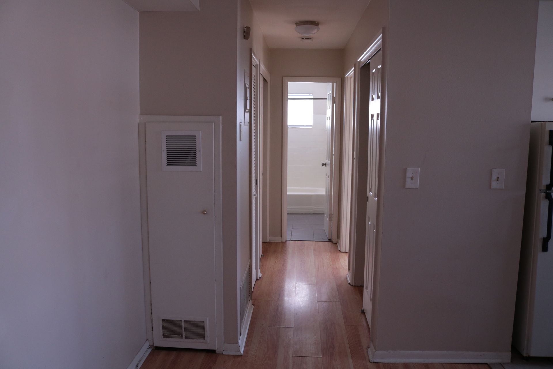 Hallway with wood floors, two doors on the right, one on the left, and a bathroom at the end.