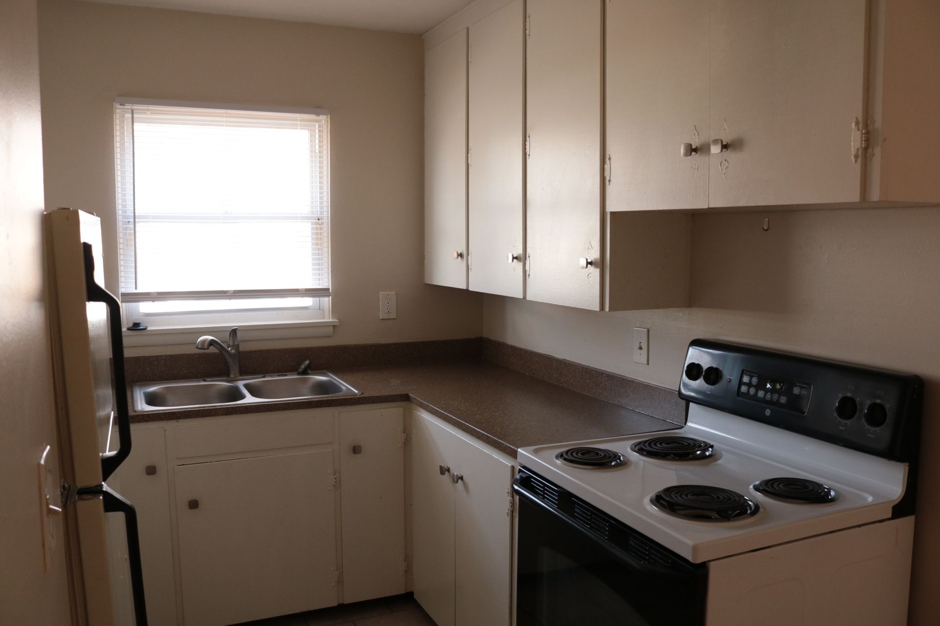 Small kitchen with white cabinets, appliances, and a window.