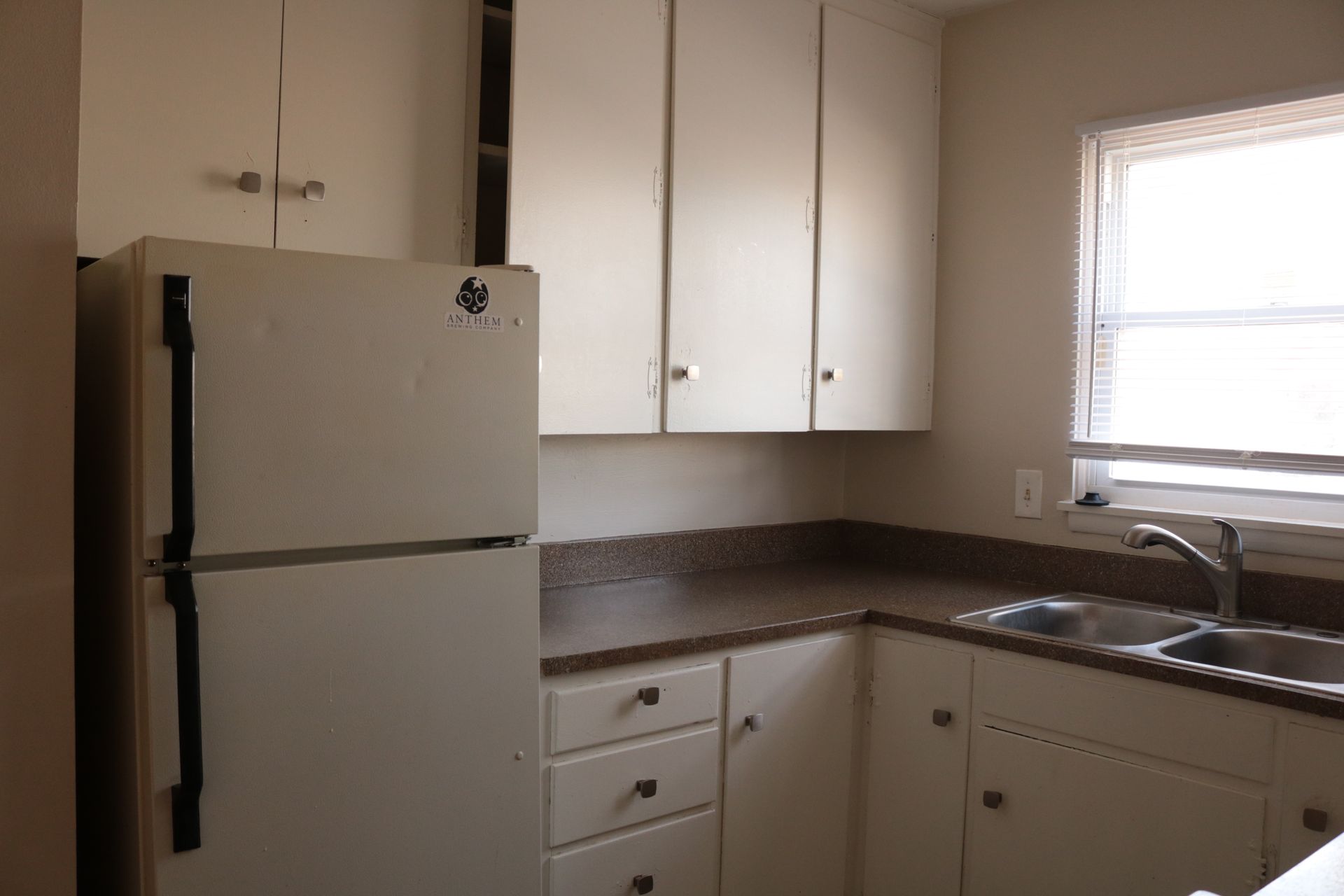 Kitchen with white cabinets, countertop, refrigerator, sink, and window.