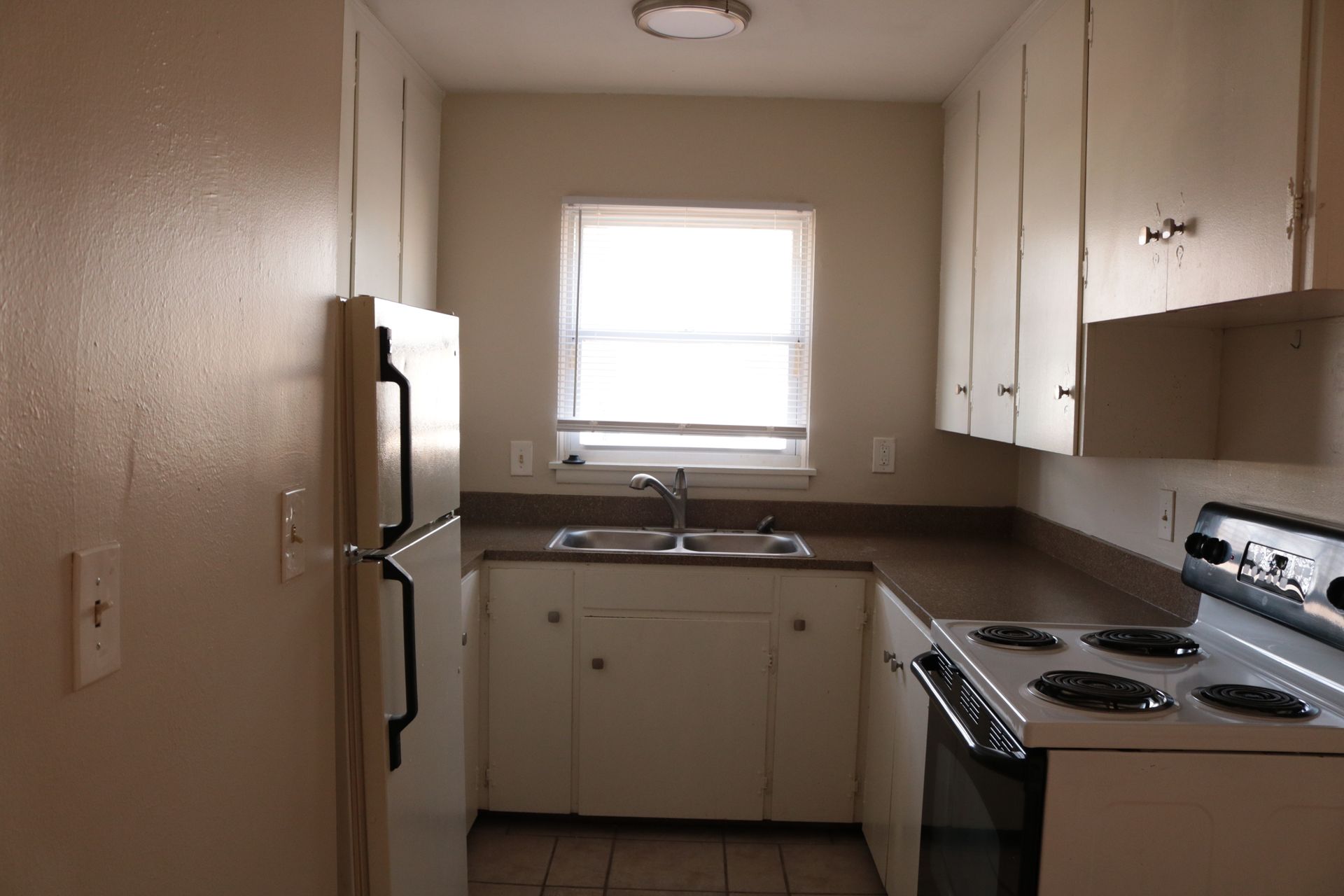 Small kitchen with white cabinets, appliances, and a window above the sink.