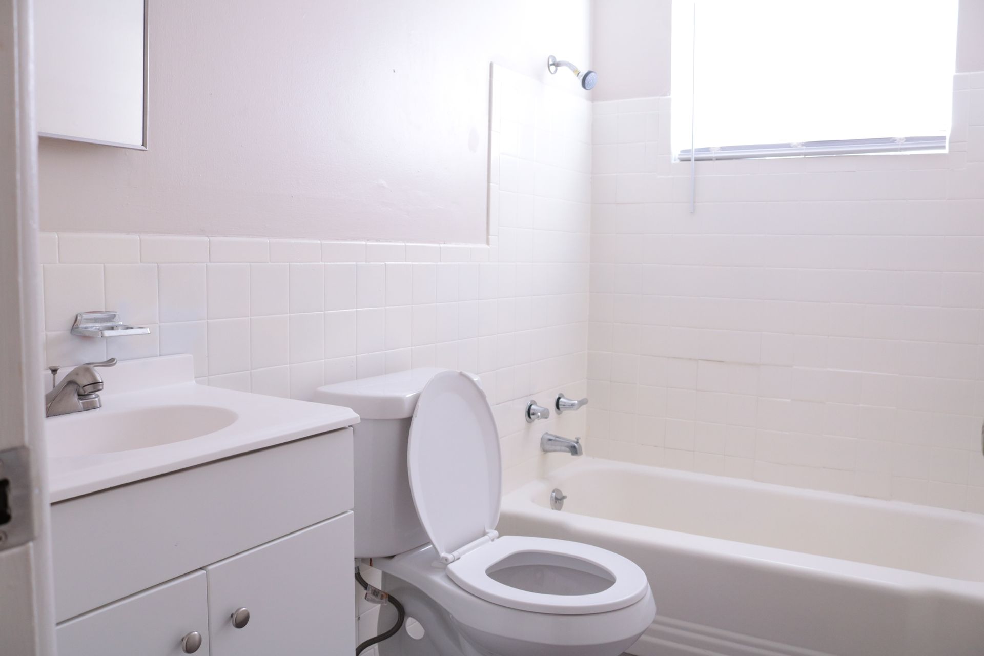 White bathroom with a sink, toilet, and bathtub. The toilet seat is up.