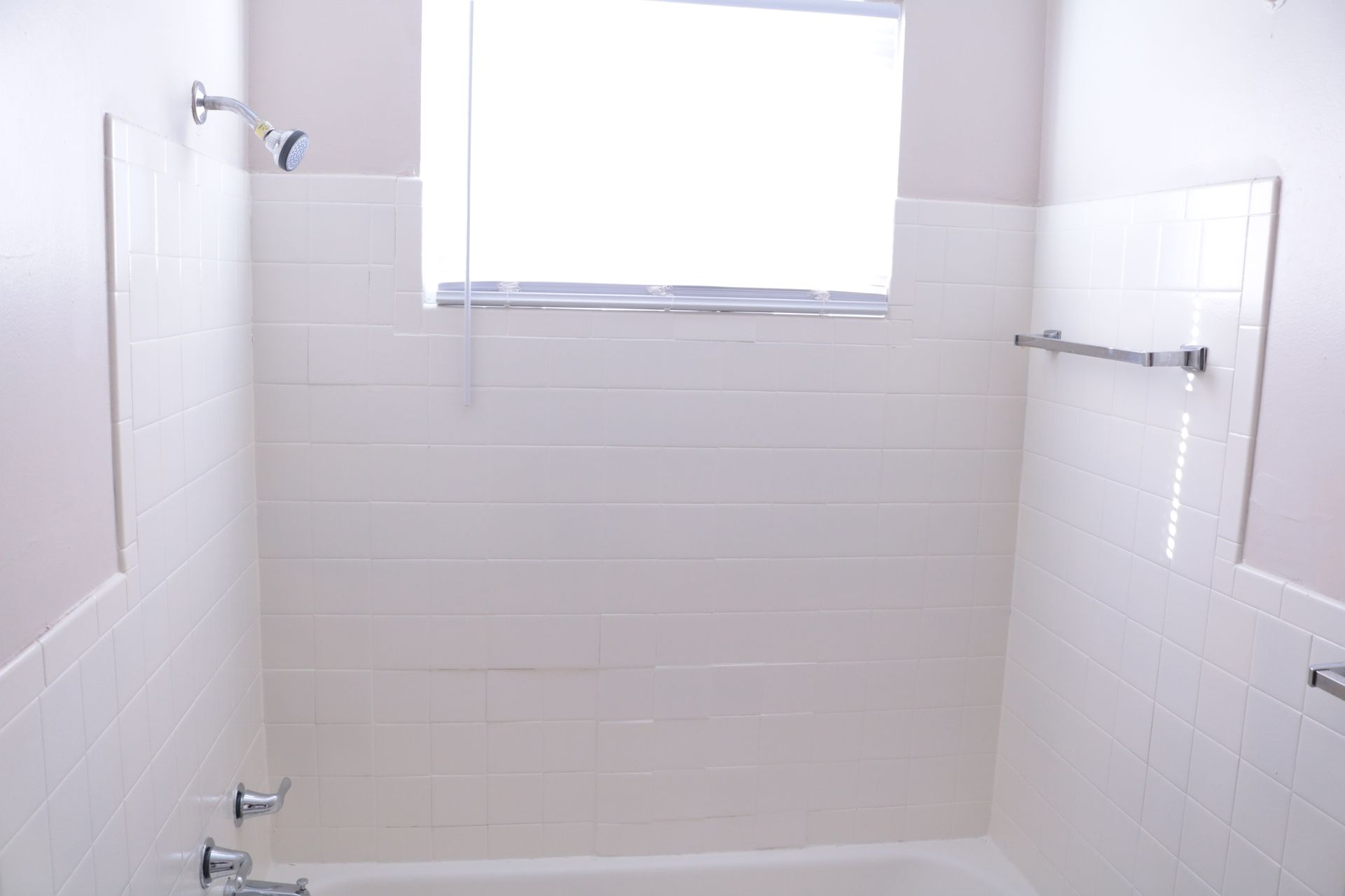 White tiled bathroom with a window, a shower head, and a towel rack.