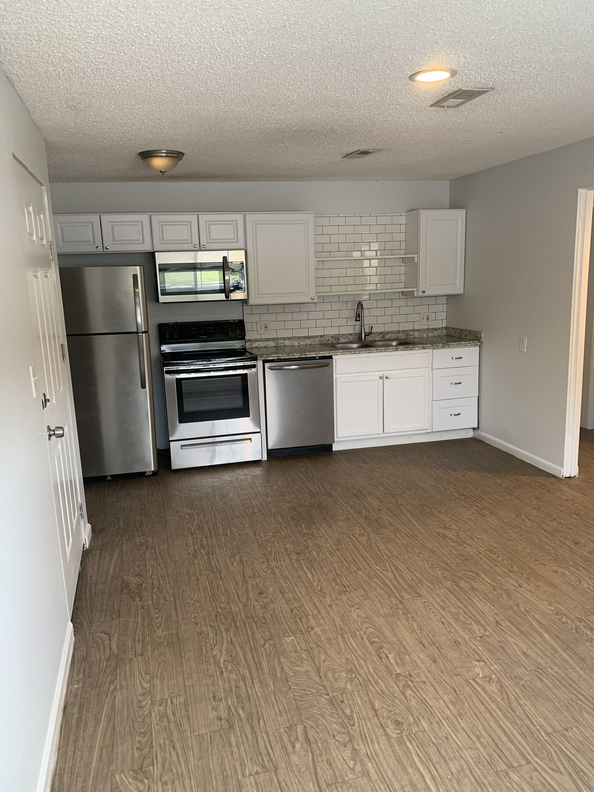 Kitchen with white cabinets, stainless steel appliances, and wood-look flooring.