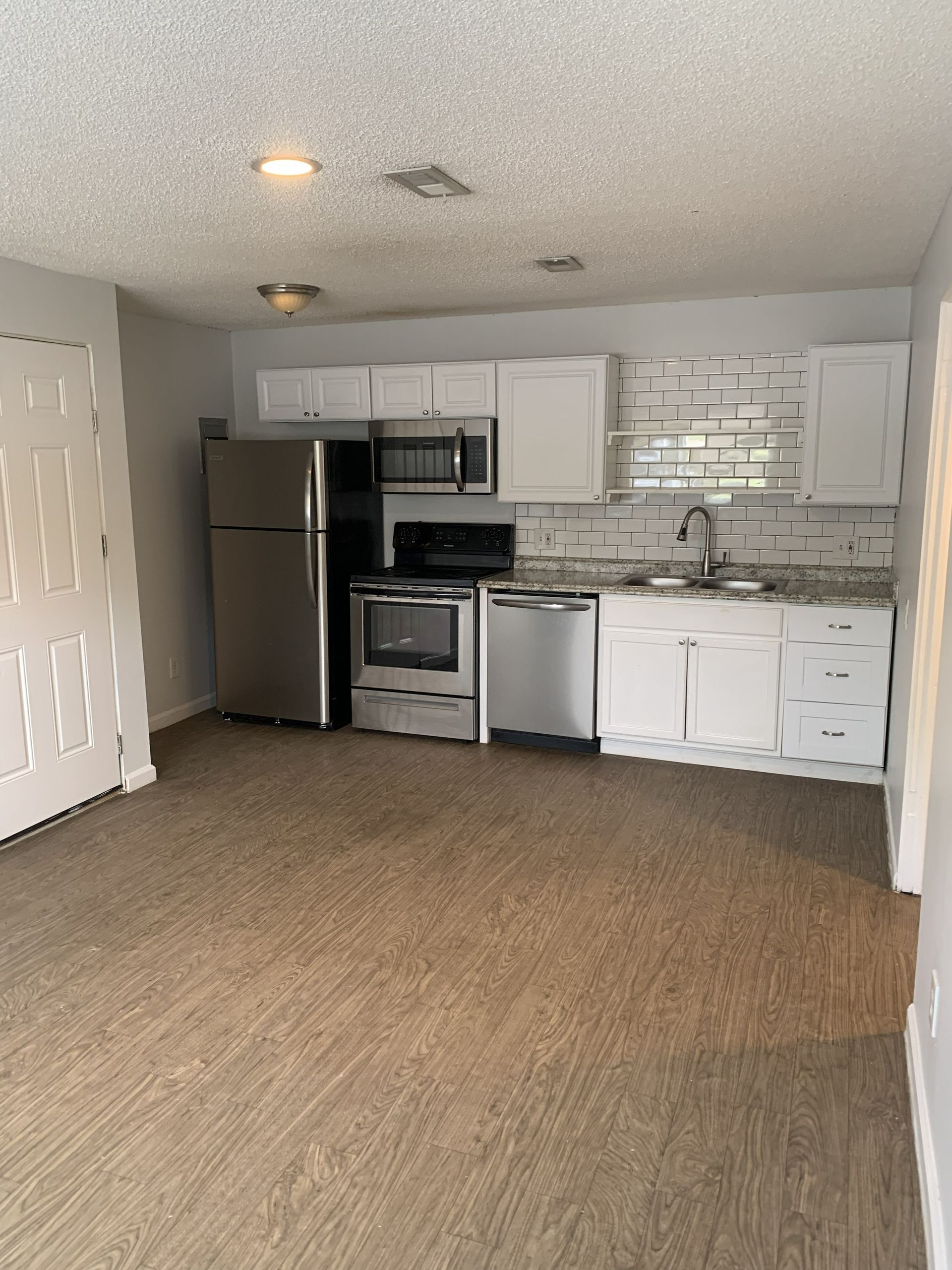 Kitchen with stainless steel appliances, white cabinets, and patterned backsplash. Brown carpet.