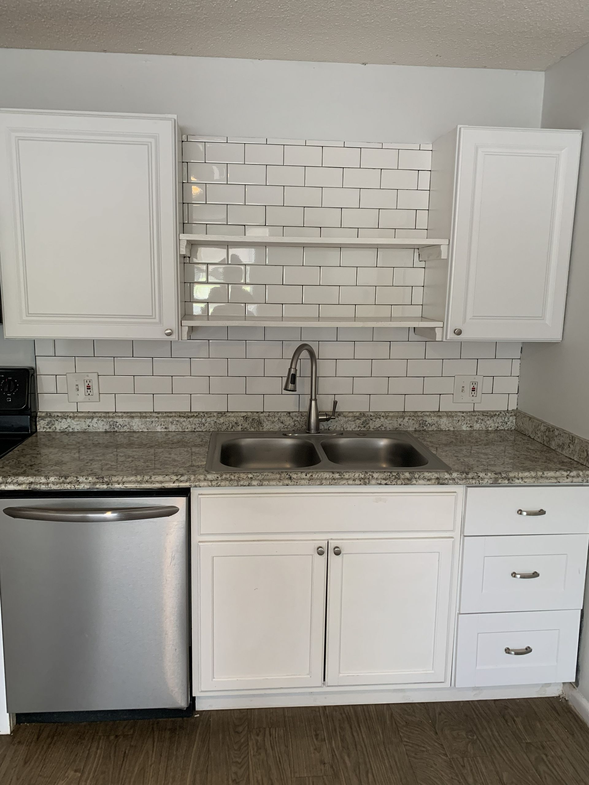 White kitchen cabinets and backsplash with stainless steel appliances and double sink.