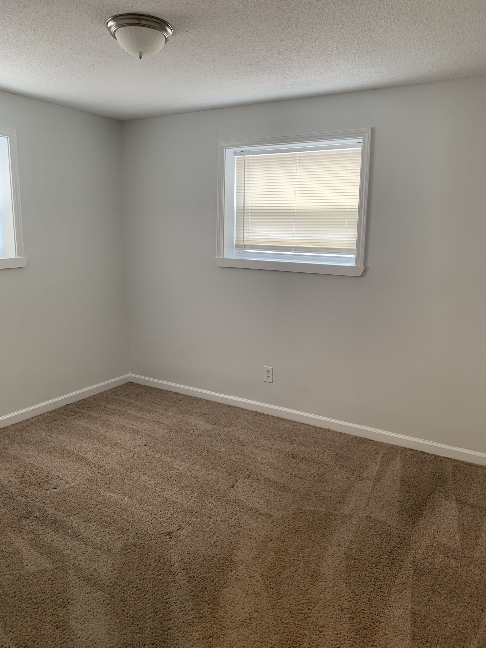 Empty room with brown carpet, white walls, and a window with blinds.