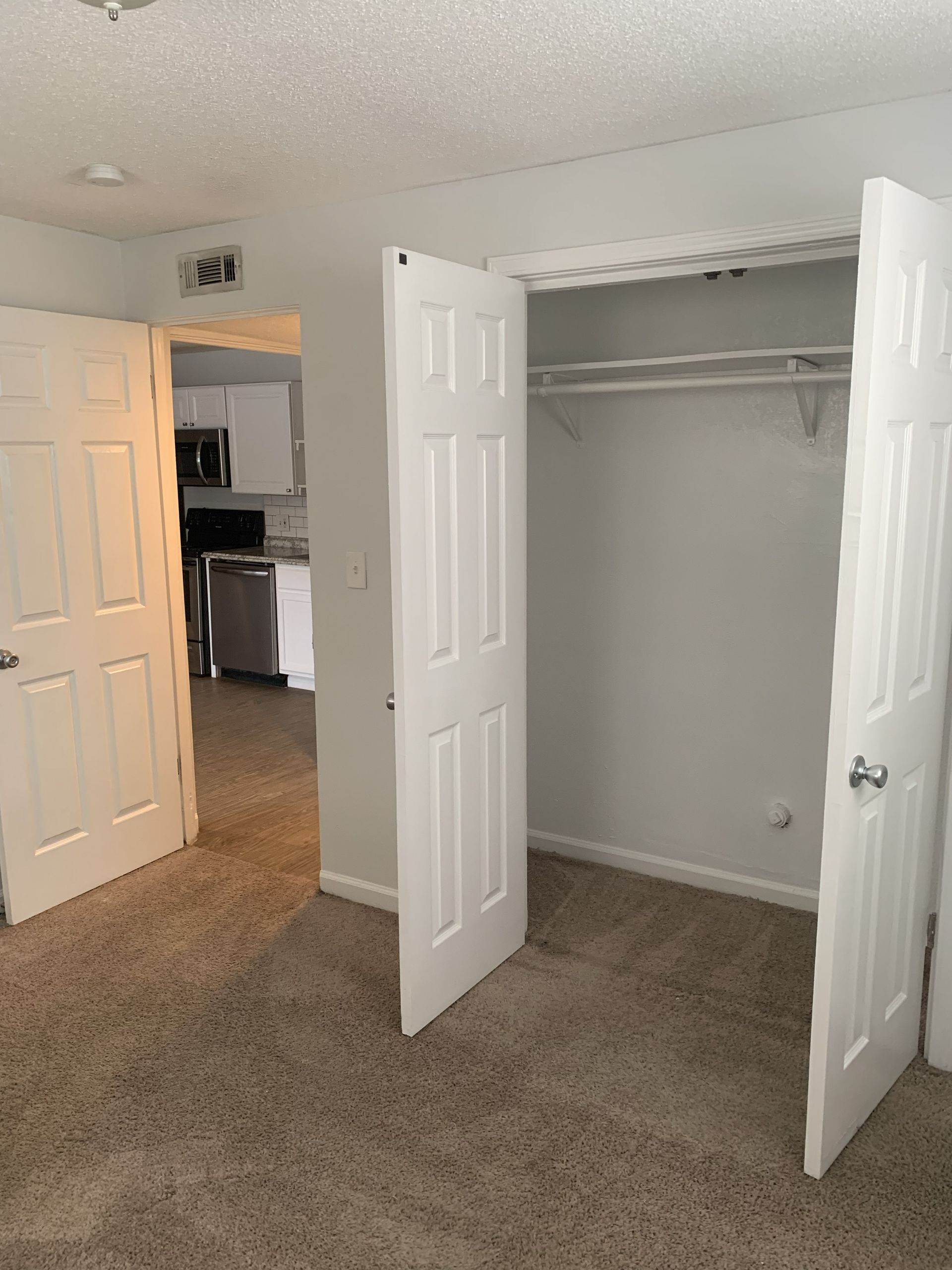 Bedroom with open closet and doorway to kitchen.
