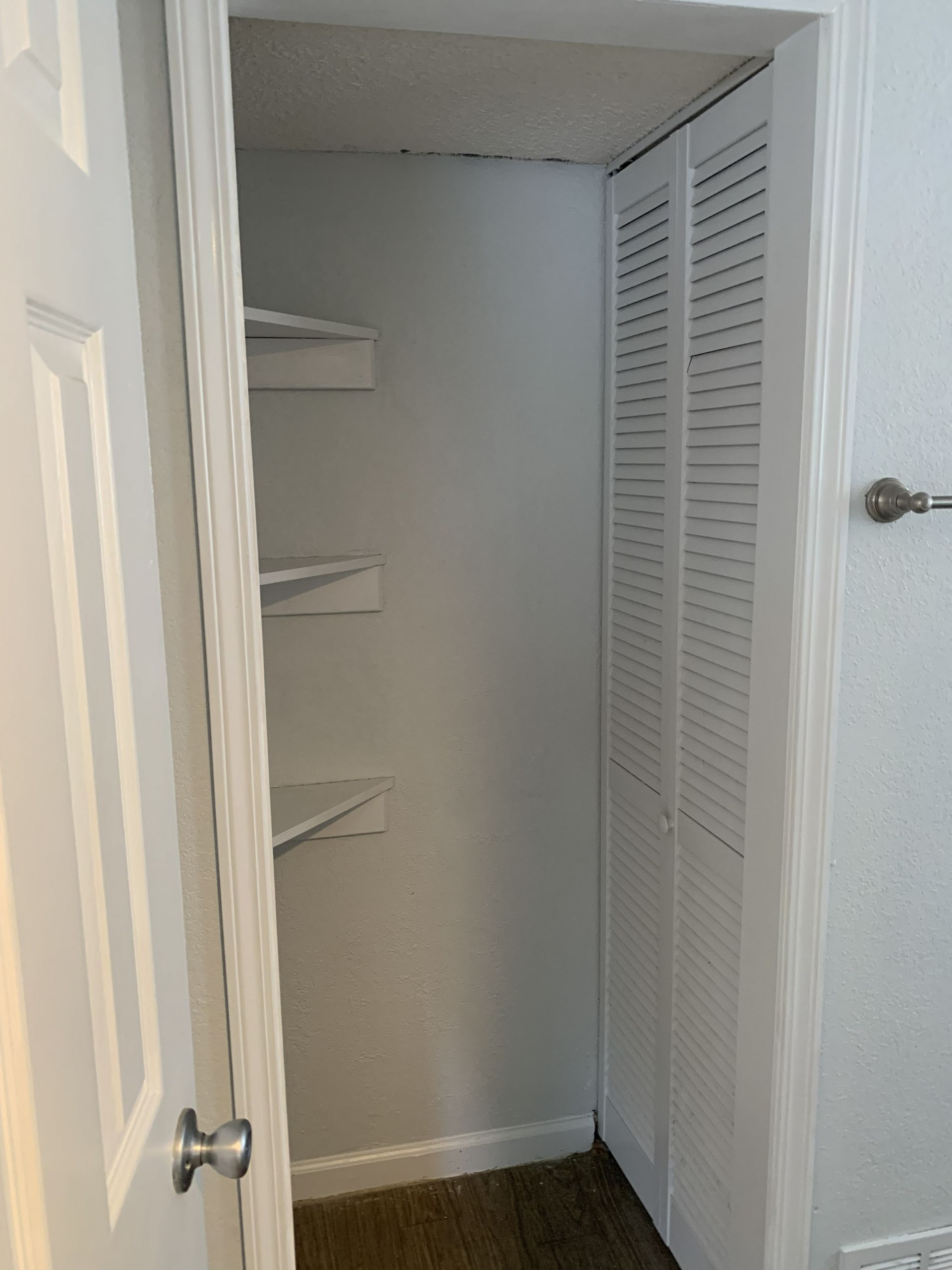 White closet with shelves and bi-fold doors, next to a white wall with a towel rack.