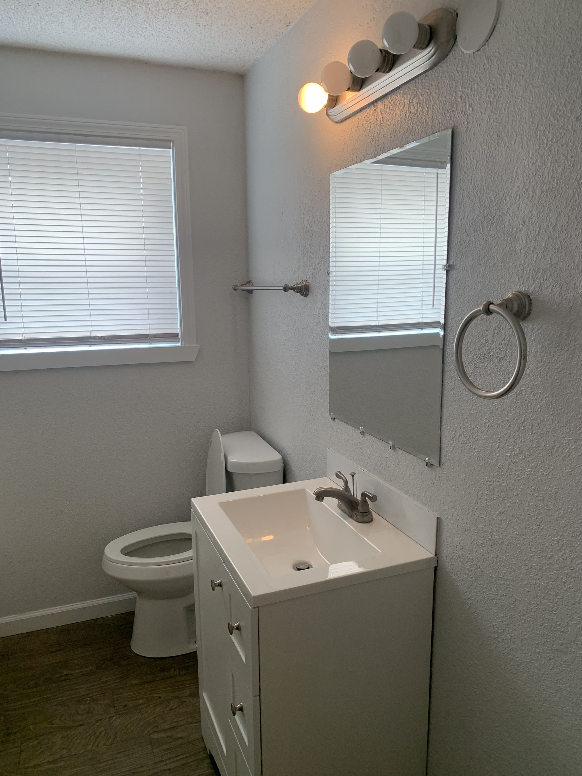 Small bathroom with a toilet, vanity, mirror, and window with blinds.