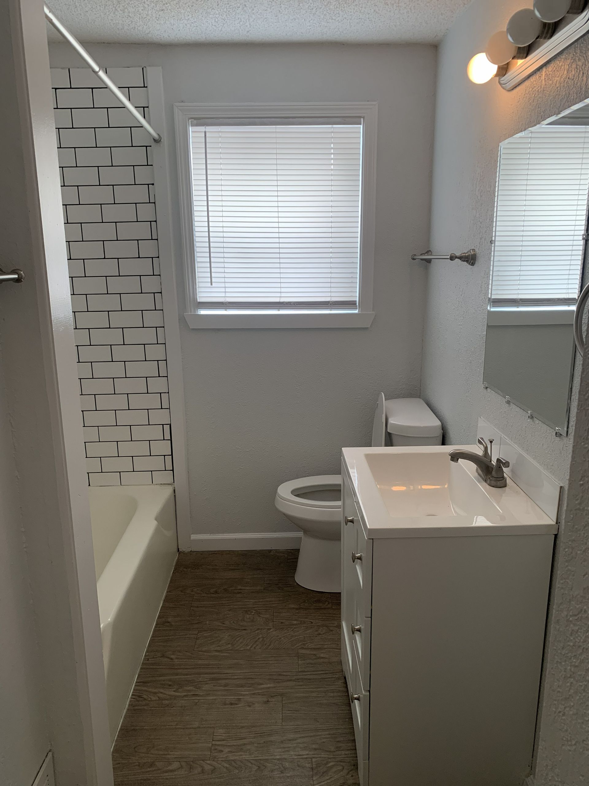 Bathroom with a white vanity, toilet, and bathtub with a patterned tile wall.