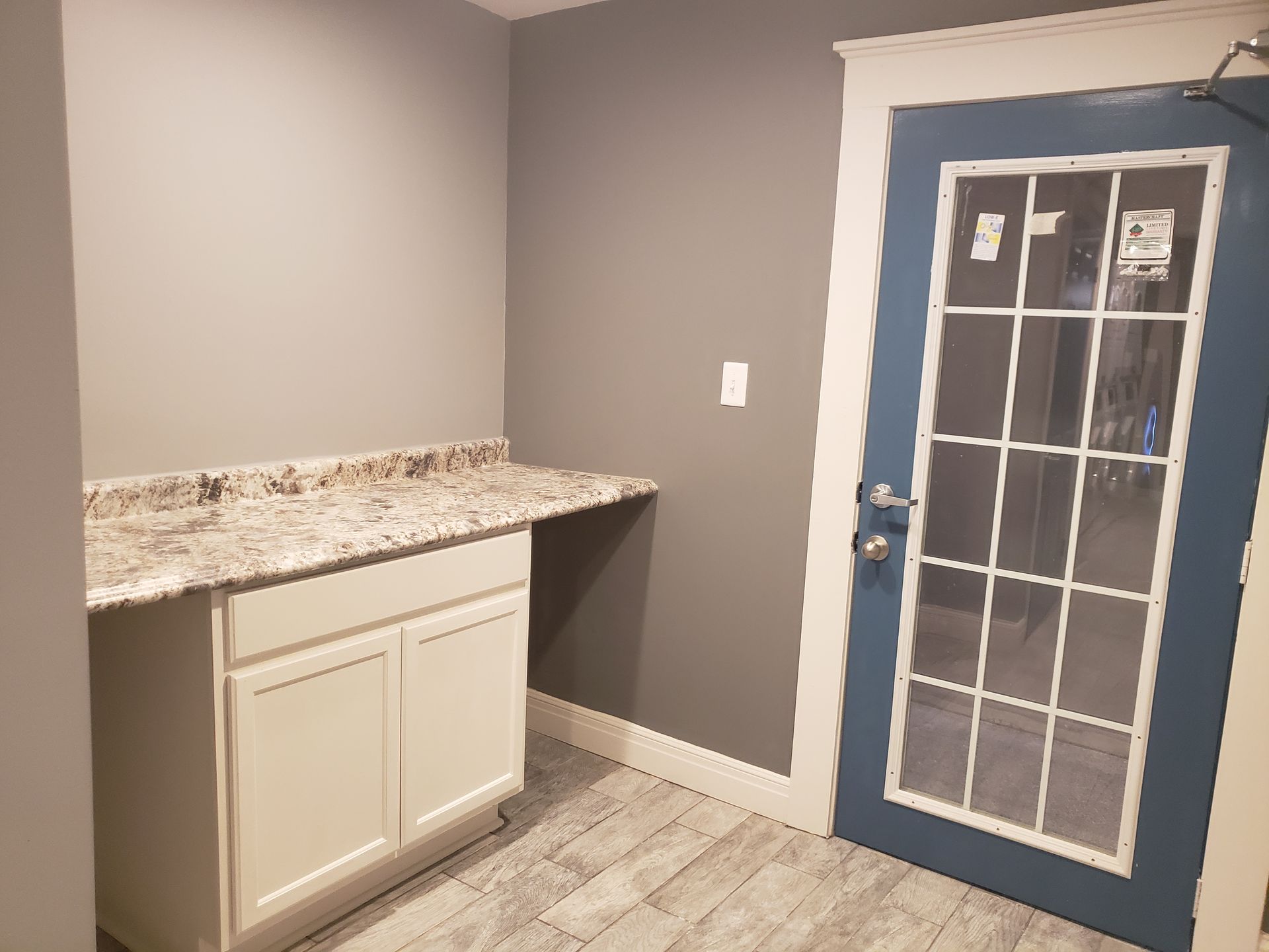 Small room with a white cabinet, a gray countertop, a blue door with a grid, and gray walls.