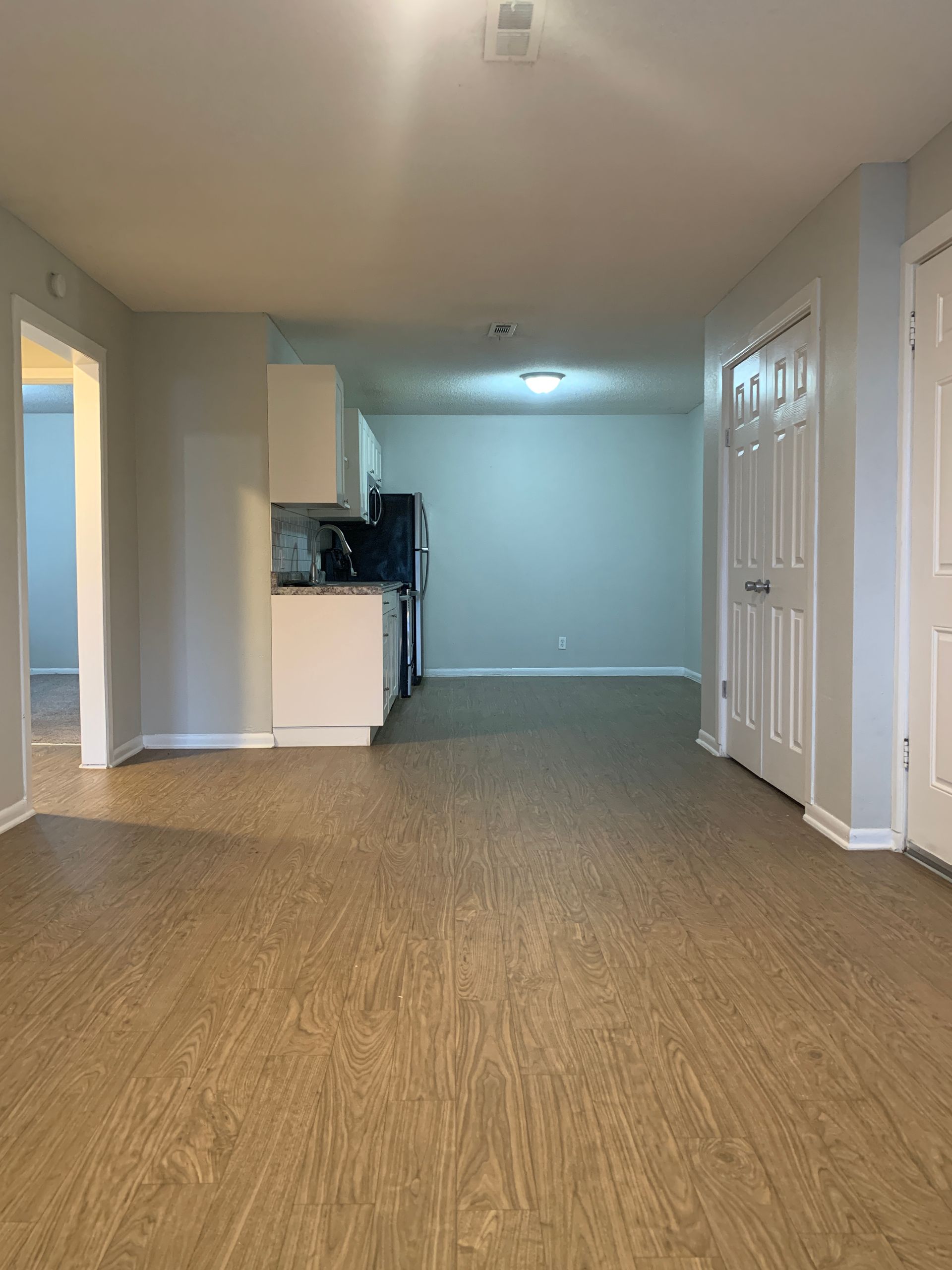 Interior view of a neutral-toned apartment, with kitchen, doors, and laminate flooring.