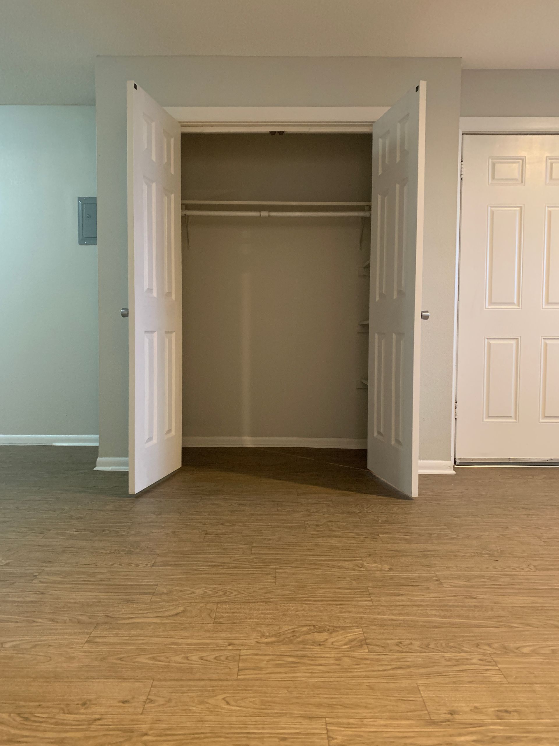 Empty closet with open white bi-fold doors, next to a closed white door, on a beige floor.