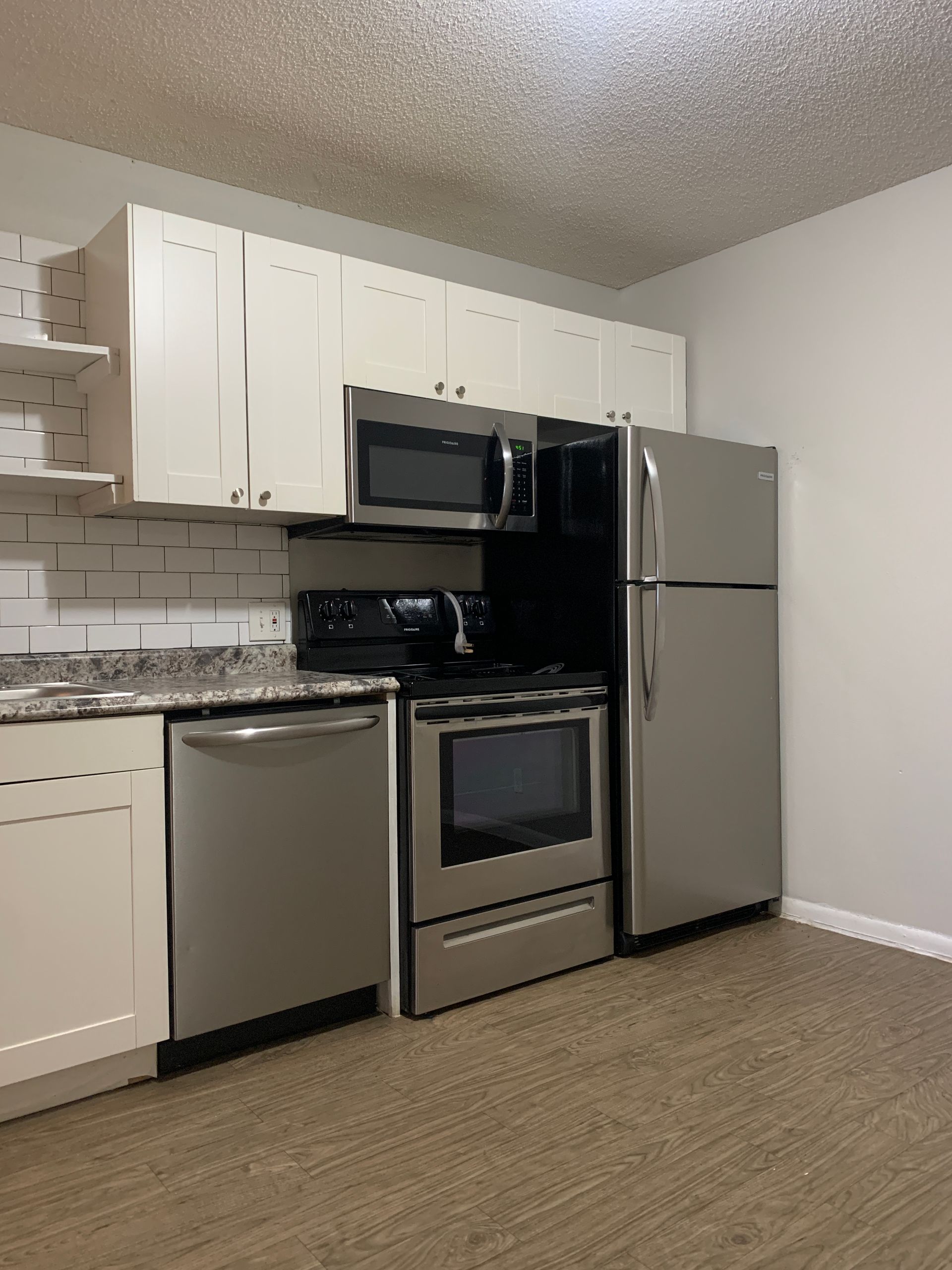 Kitchen with white cabinets, stainless steel appliances, and wood-look flooring.