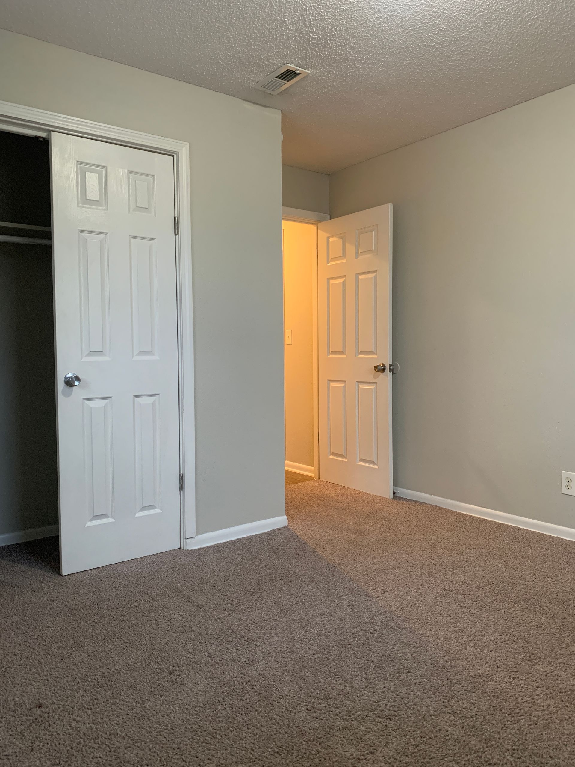 Empty bedroom with brown carpet, two white doors, and light gray walls.