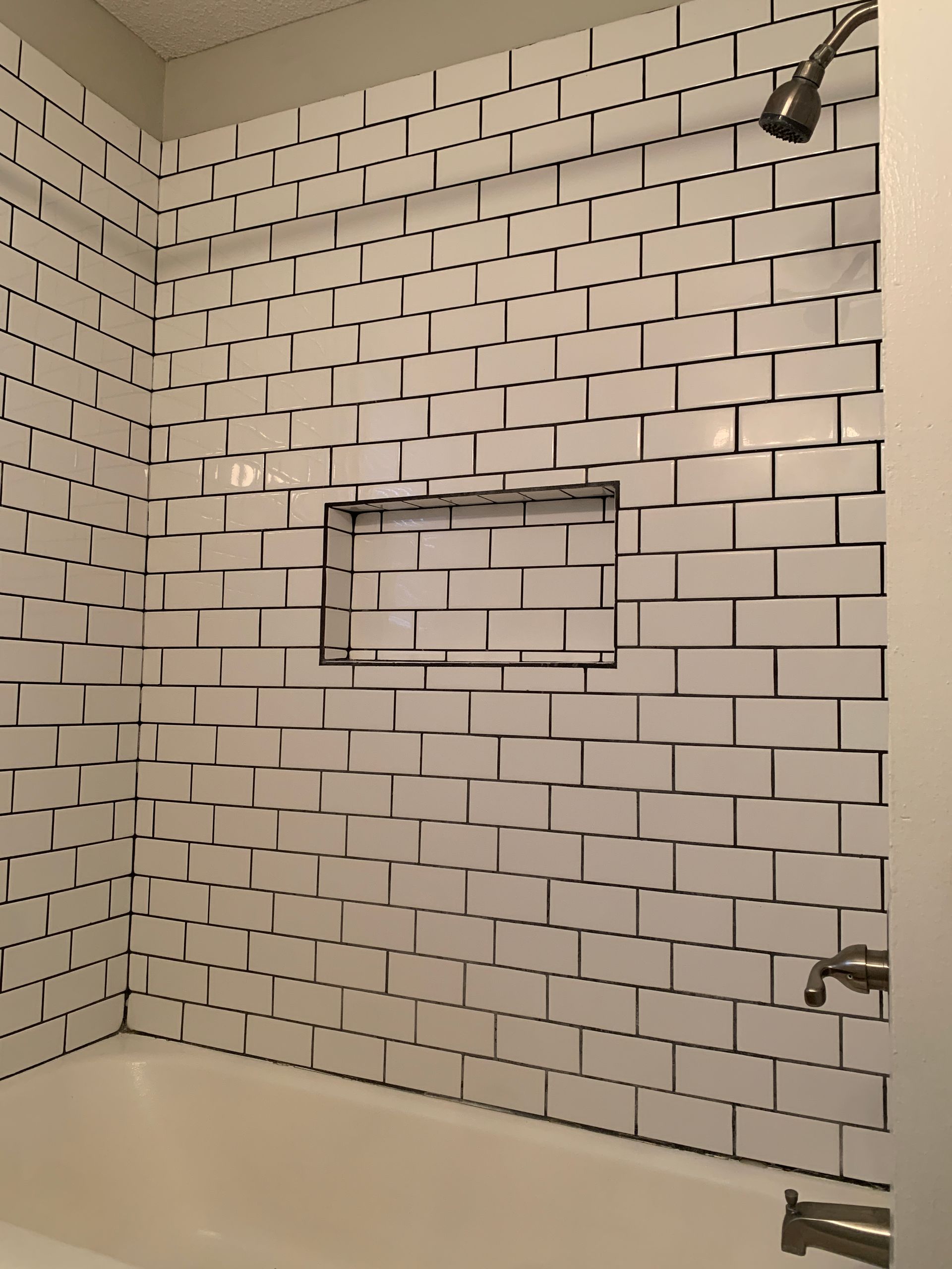 White subway tile shower with recessed shelf and silver fixtures.